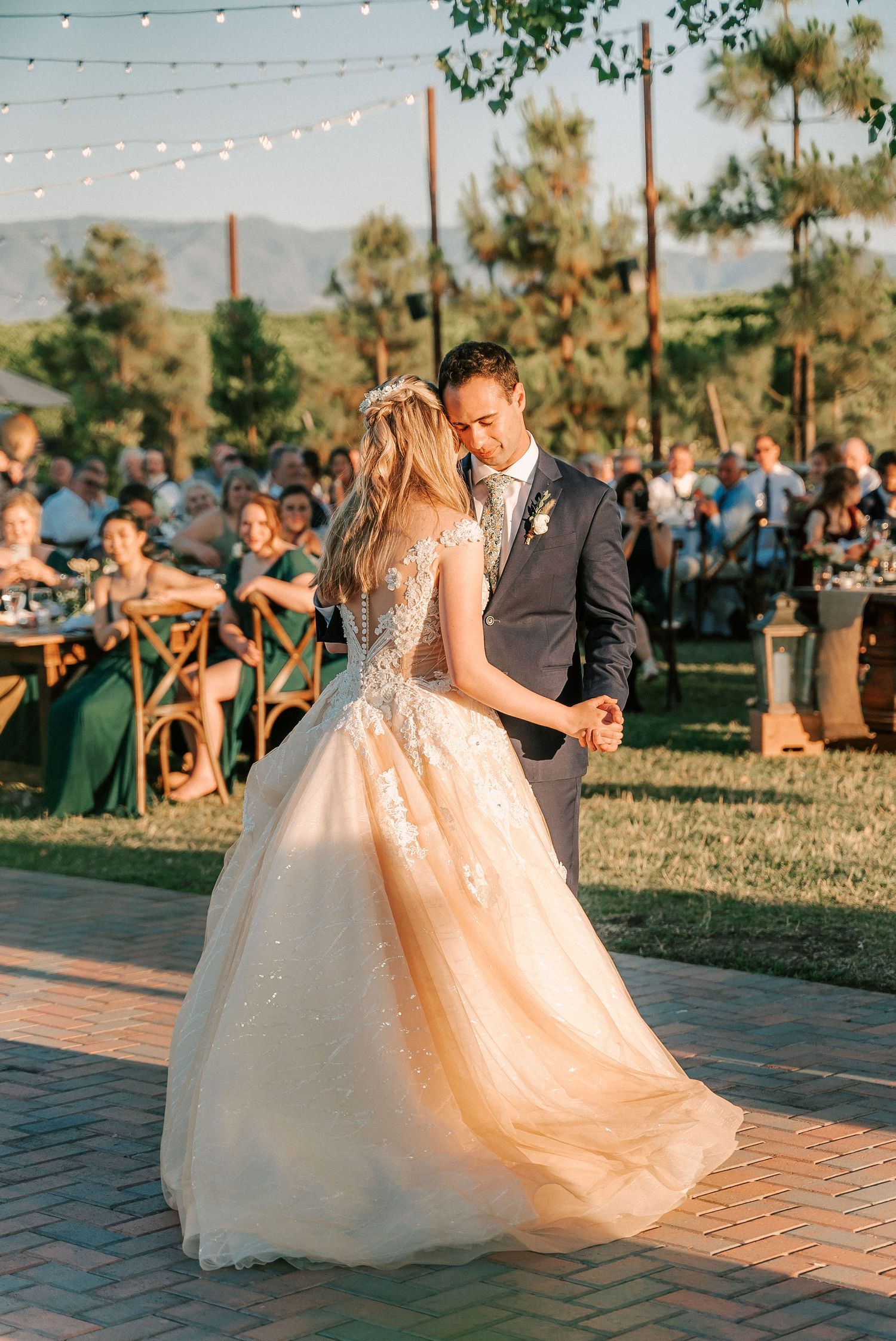 Bride and groom share their first dance outdoors at a romantic wedding reception with string lights and mountain views.