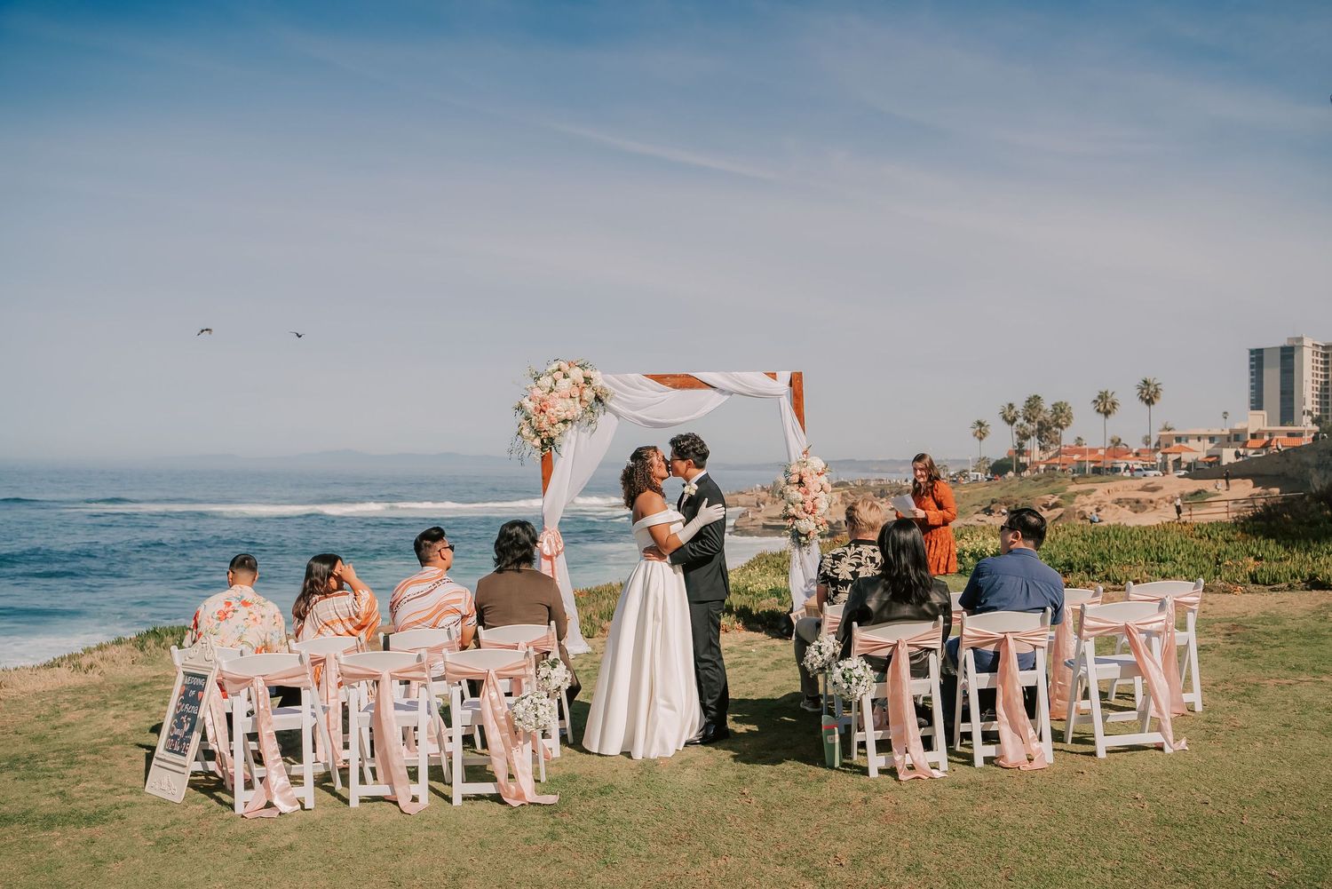 Couple kissing at outdoor beach wedding ceremony with ocean view.