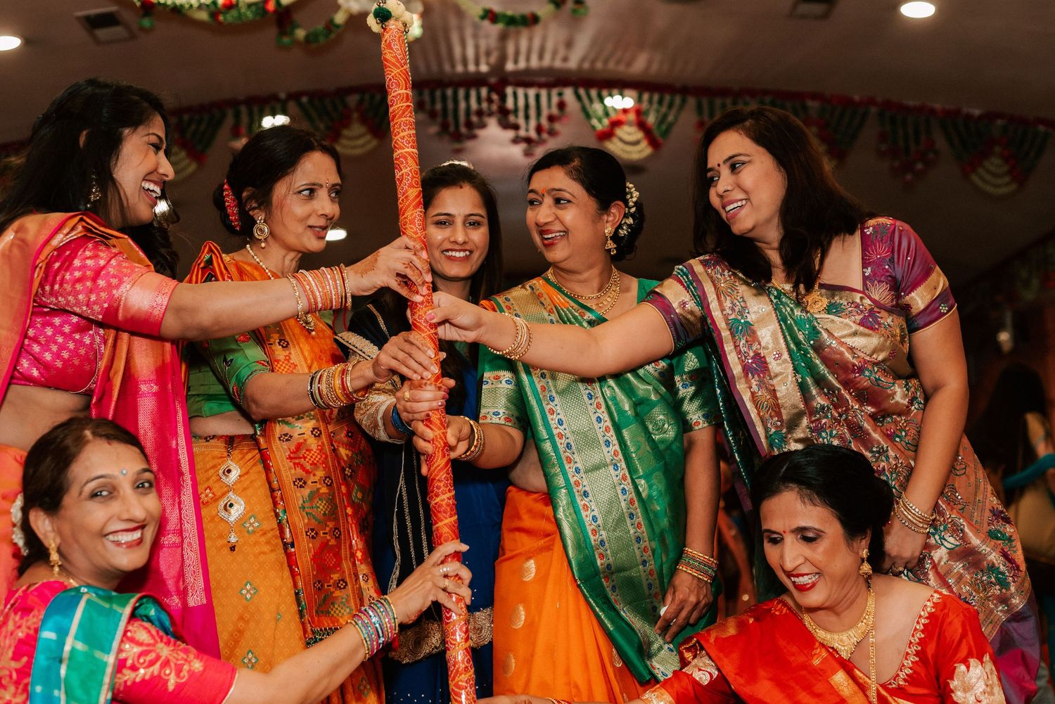 Group of women in vibrant sarees laughing and celebrating together during an Indian wedding ceremony.