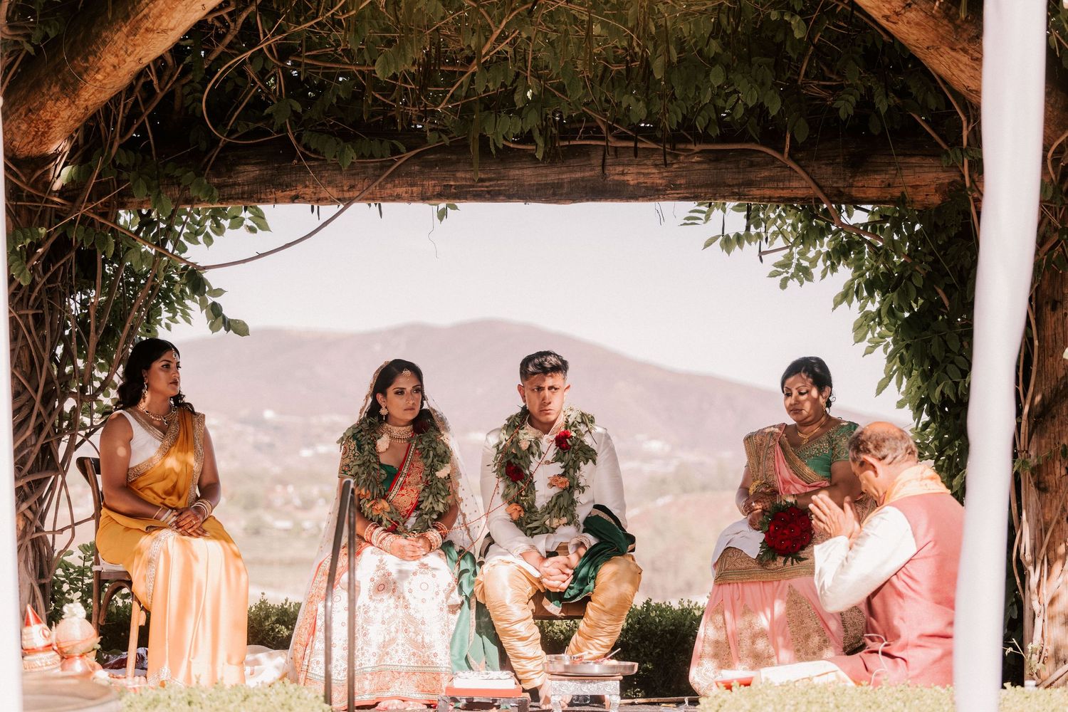 Indian wedding ceremony couple seated under rustic pergola with mountain views.