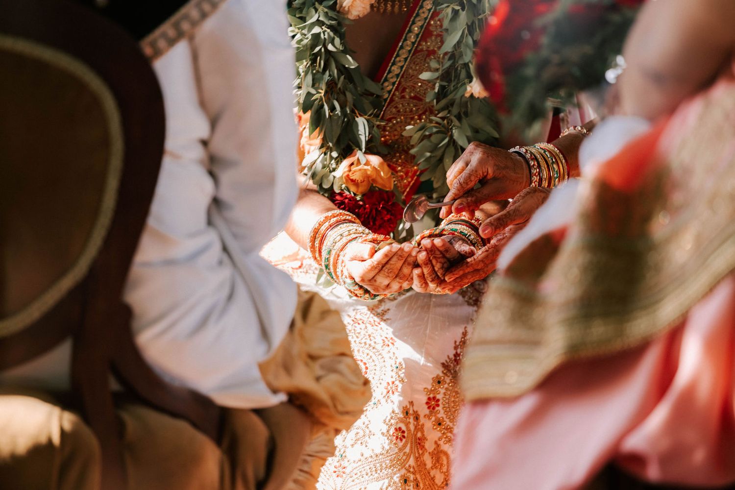 Close-up of Indian bride and groom\u2019s hands adorned with mehndi and bangles during Hindu wedding ceremony.
