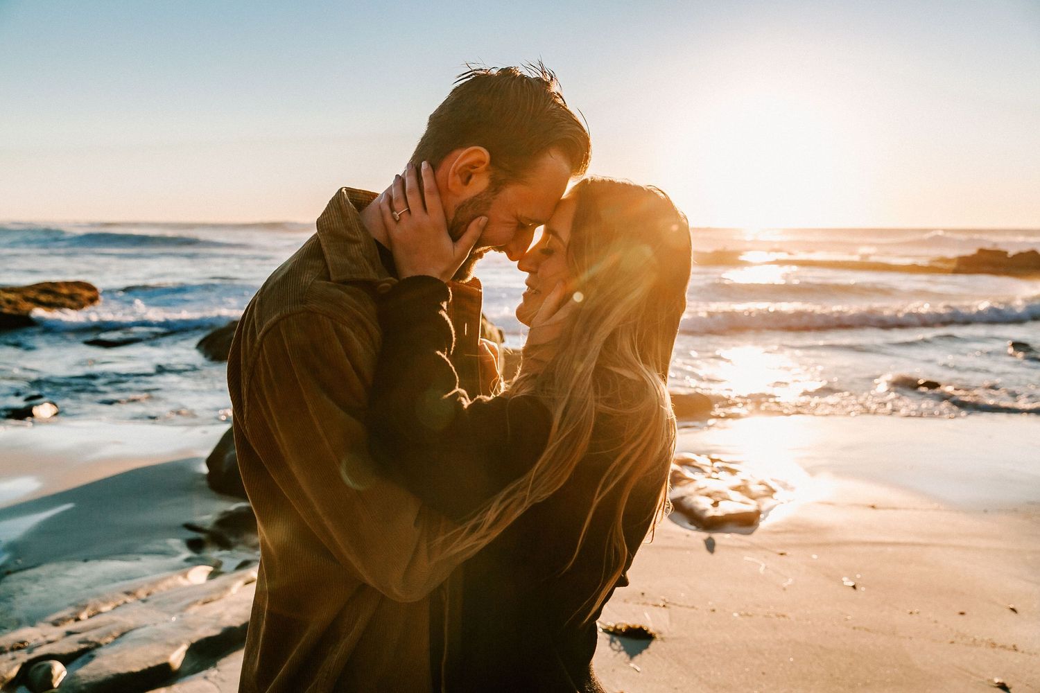 Couple sharing an intimate moment on beach at golden sunset, foreheads touching tenderly.
