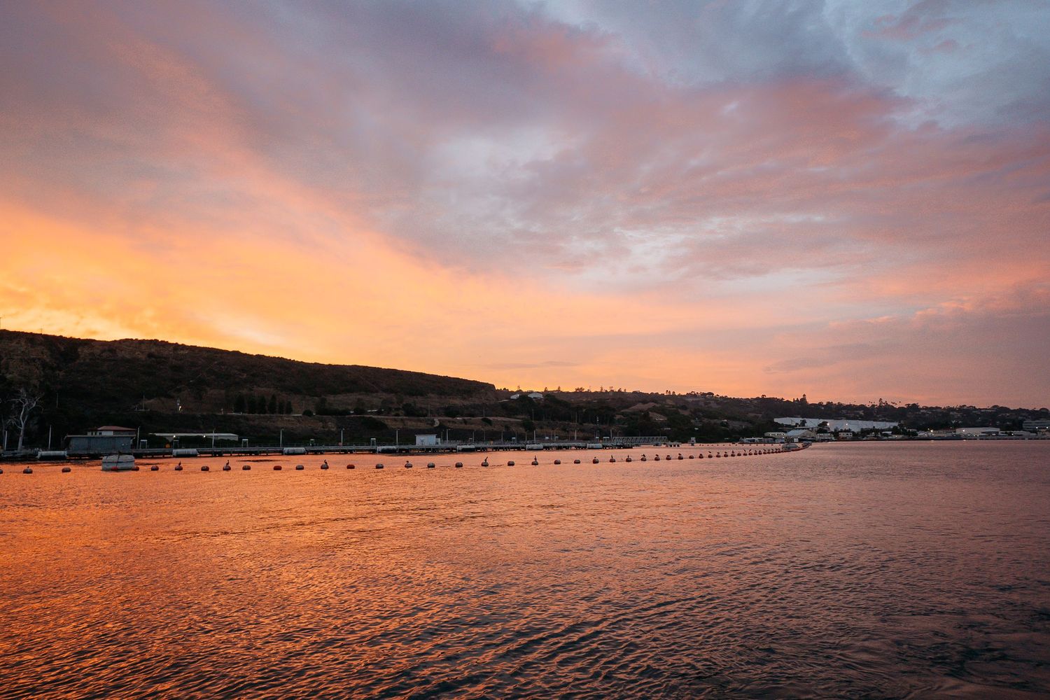 Stunning sunset over a coastal harbor with vibrant orange and pink skies reflecting on calm water.