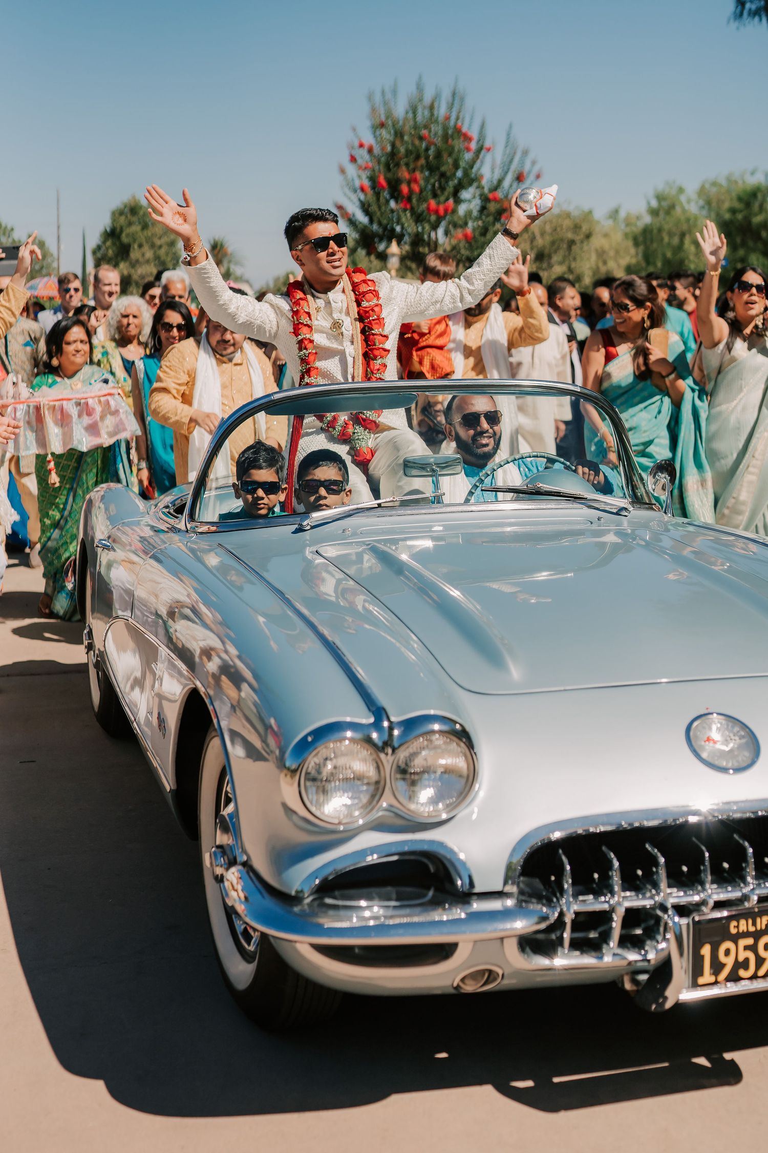 Groom celebrates in vintage 1959 Corvette convertible during Indian wedding baraat procession.