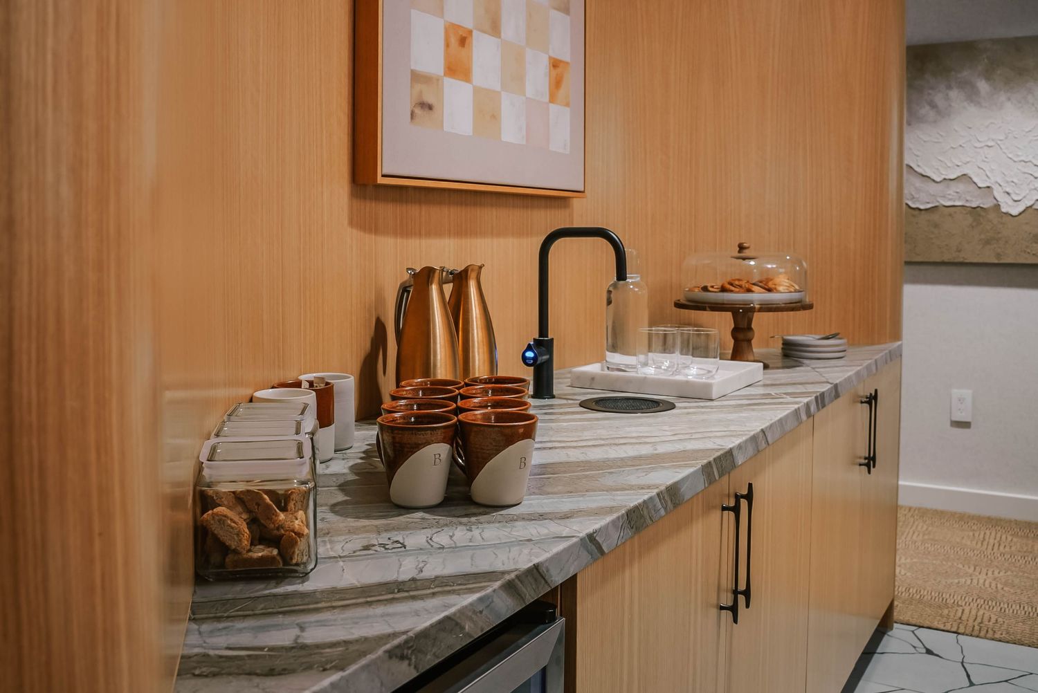 Modern kitchen counter with marble surface, black faucet, wooden accents, and elegant decor in a warm-toned space.