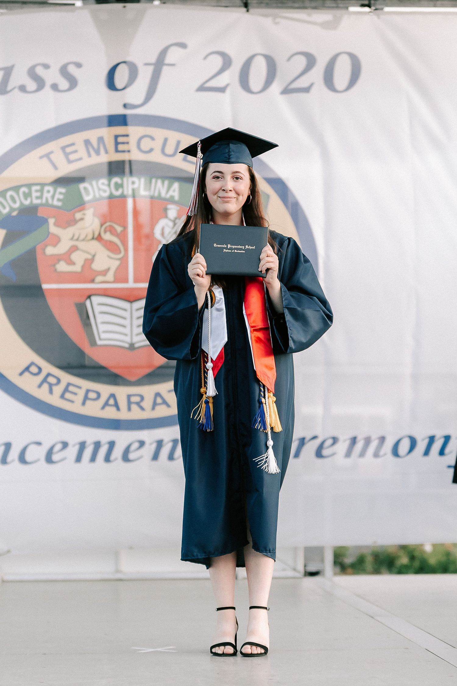 Graduate in cap and gown holds diploma at Temecula Preparatory Class of 2020 commencement ceremony.