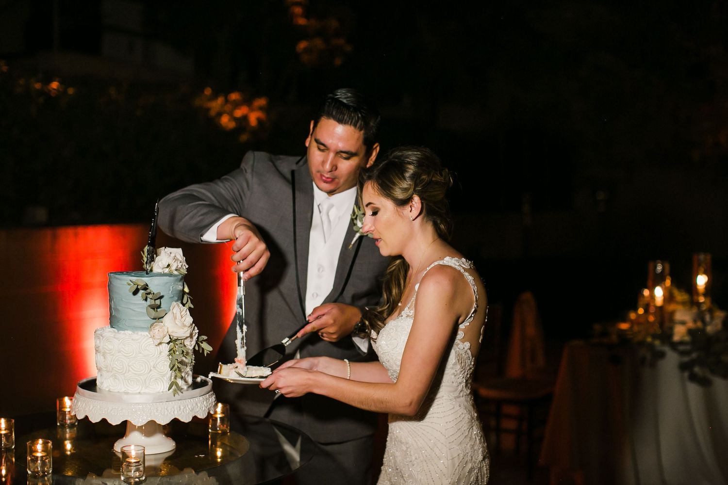 Bride and groom cutting their elegant white wedding cake together at an outdoor evening reception.