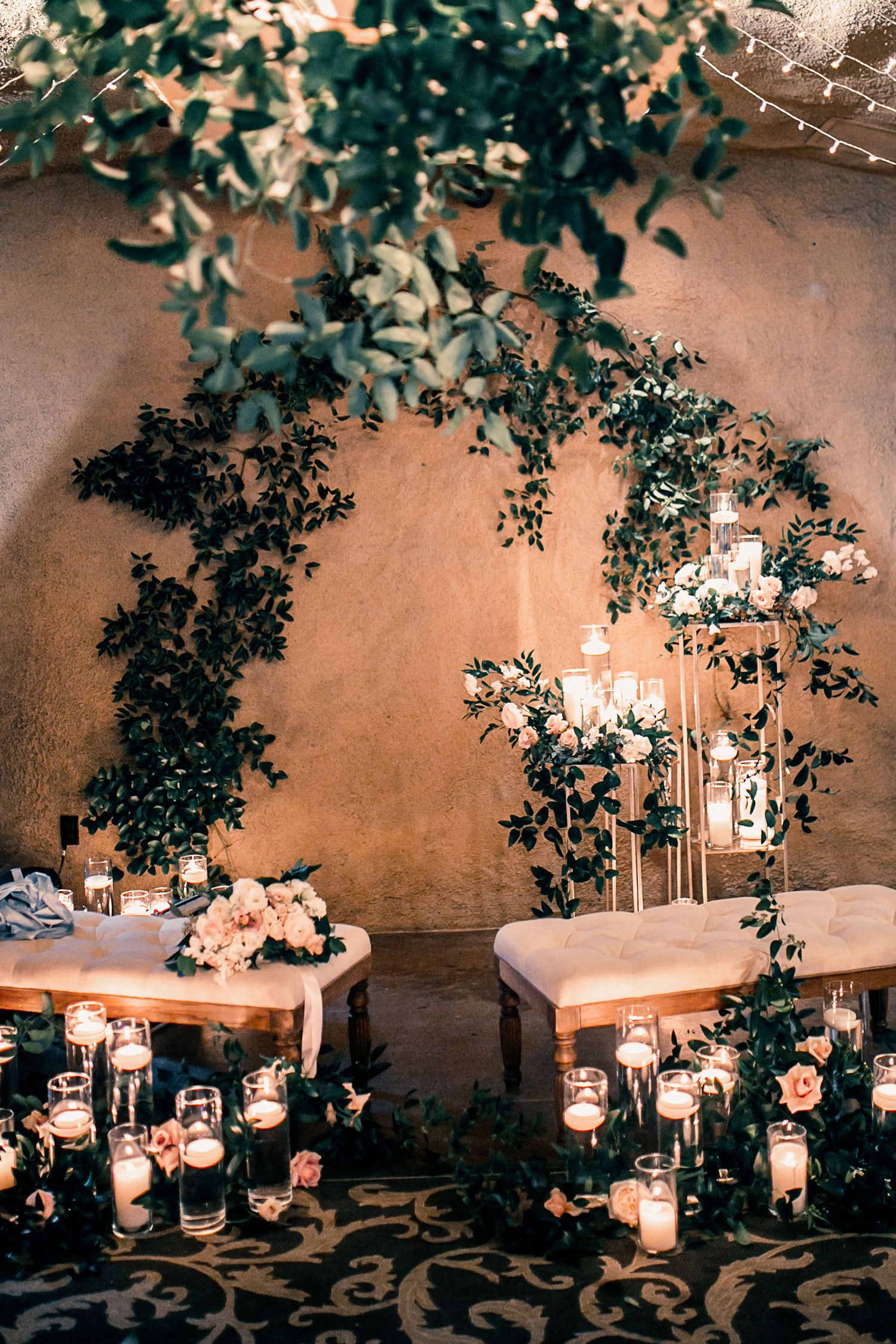 Romantic wedding sweetheart table with lush greenery arch, pillar candles, and blush floral arrangements in a warmly lit venue.