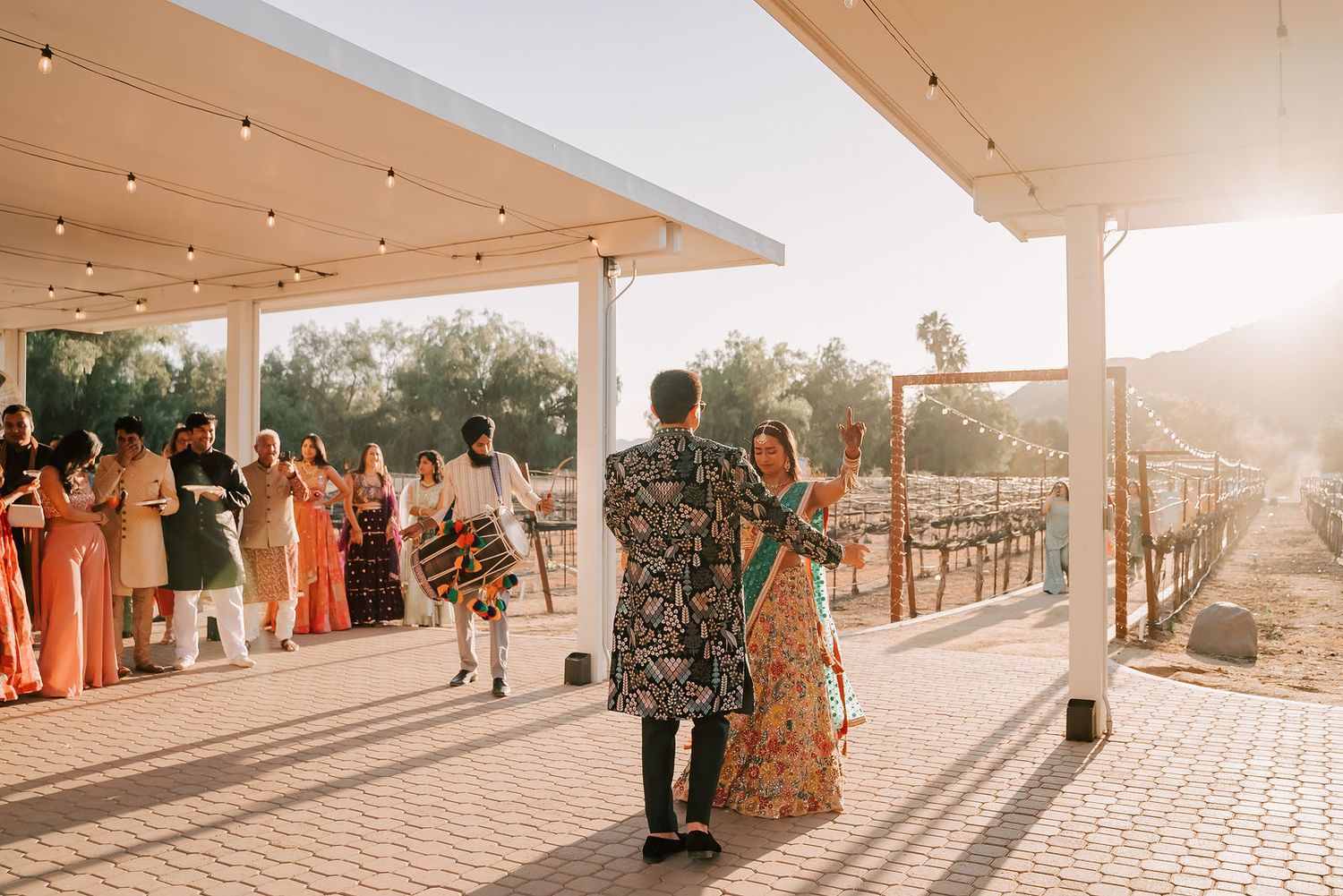 Couple in traditional Indian attire welcomed by guests at a golden hour outdoor wedding reception.