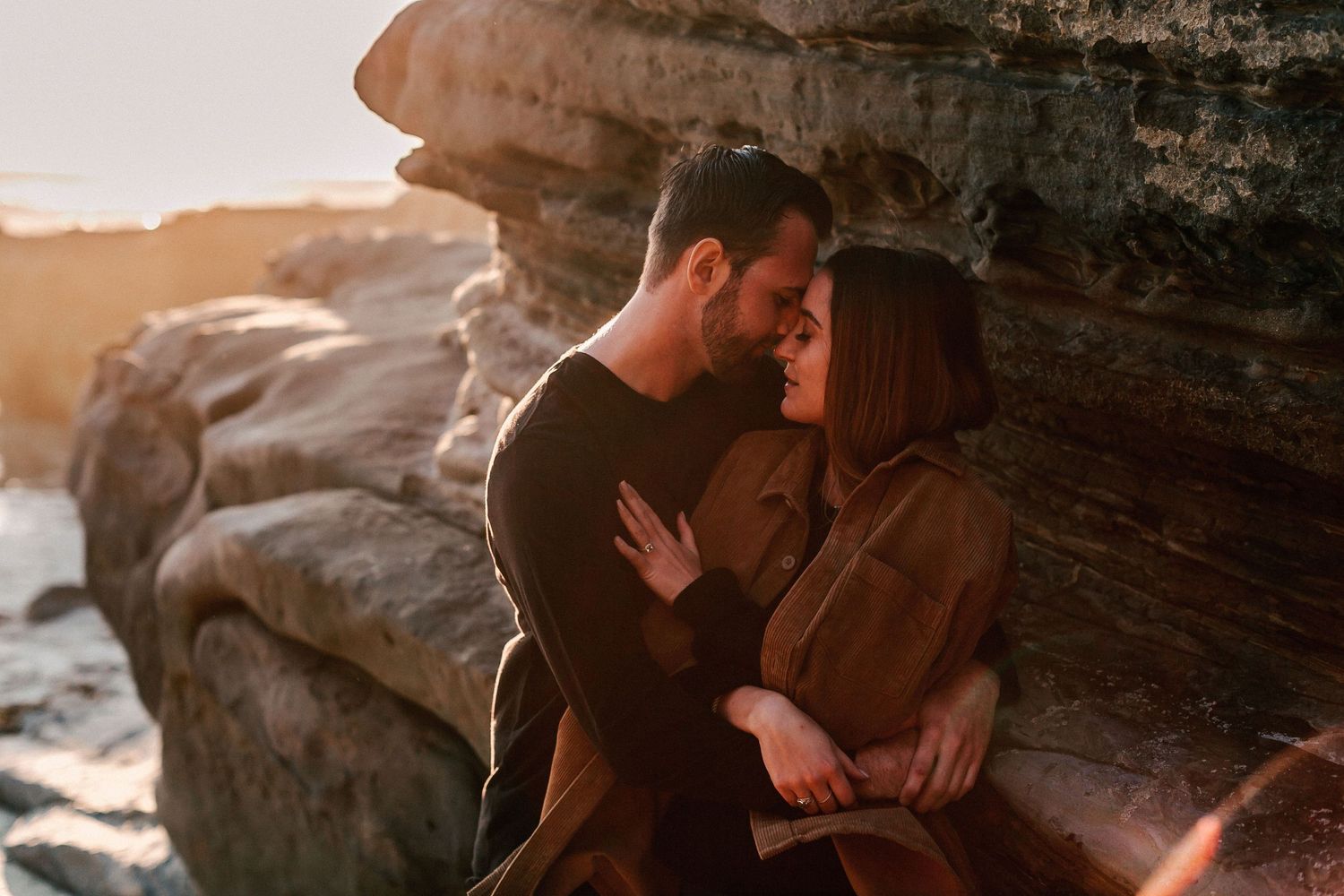 Couple sharing an intimate moment leaning against rocky cliffs at sunset.