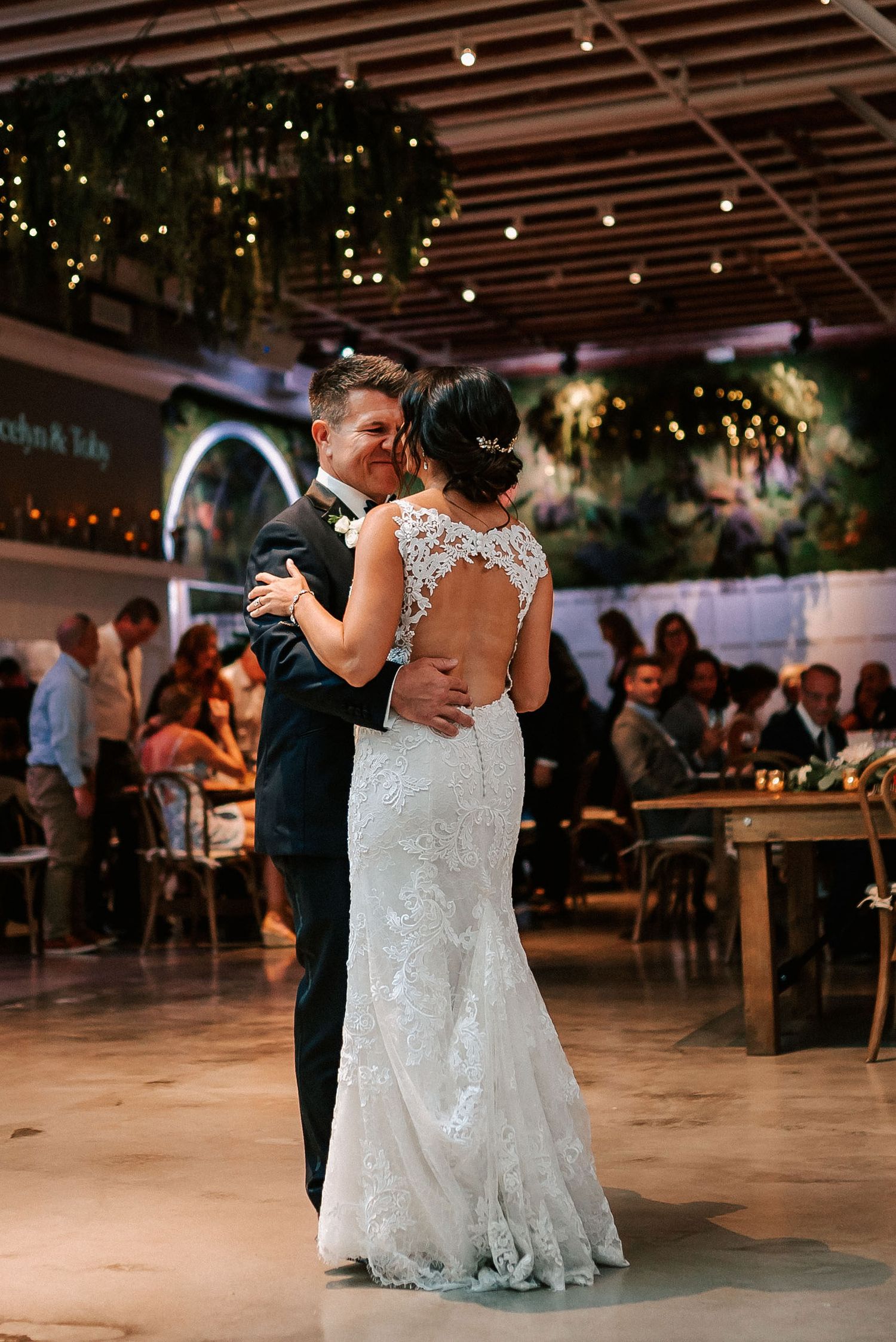Bride and groom share their first dance in a romantic venue adorned with string lights and lush greenery.