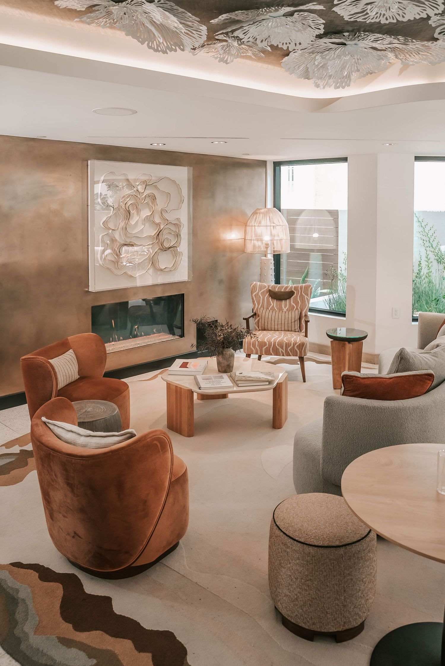 Elegant modern living room with terracotta velvet chairs, woven pendant light, abstract wall art, and decorative floral ceiling.