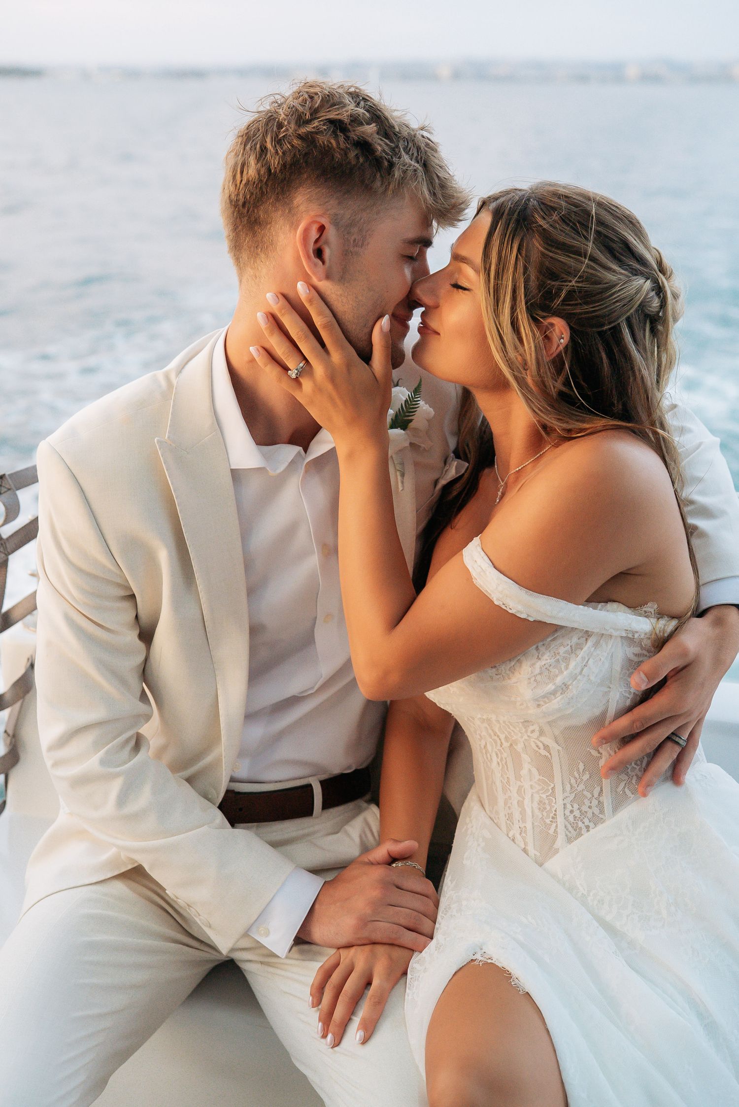 Romantic couple in wedding attire sharing a kiss by the ocean, bride in white gown and groom in beige suit.
