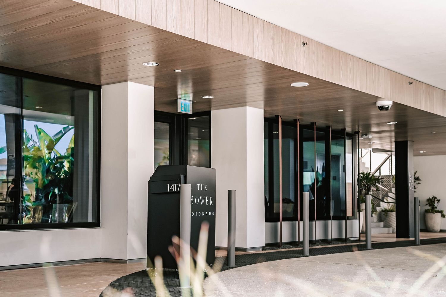 Modern hotel entrance with glass doors, wooden ceiling, and lush greenery at 1 William Street, Brisbane.