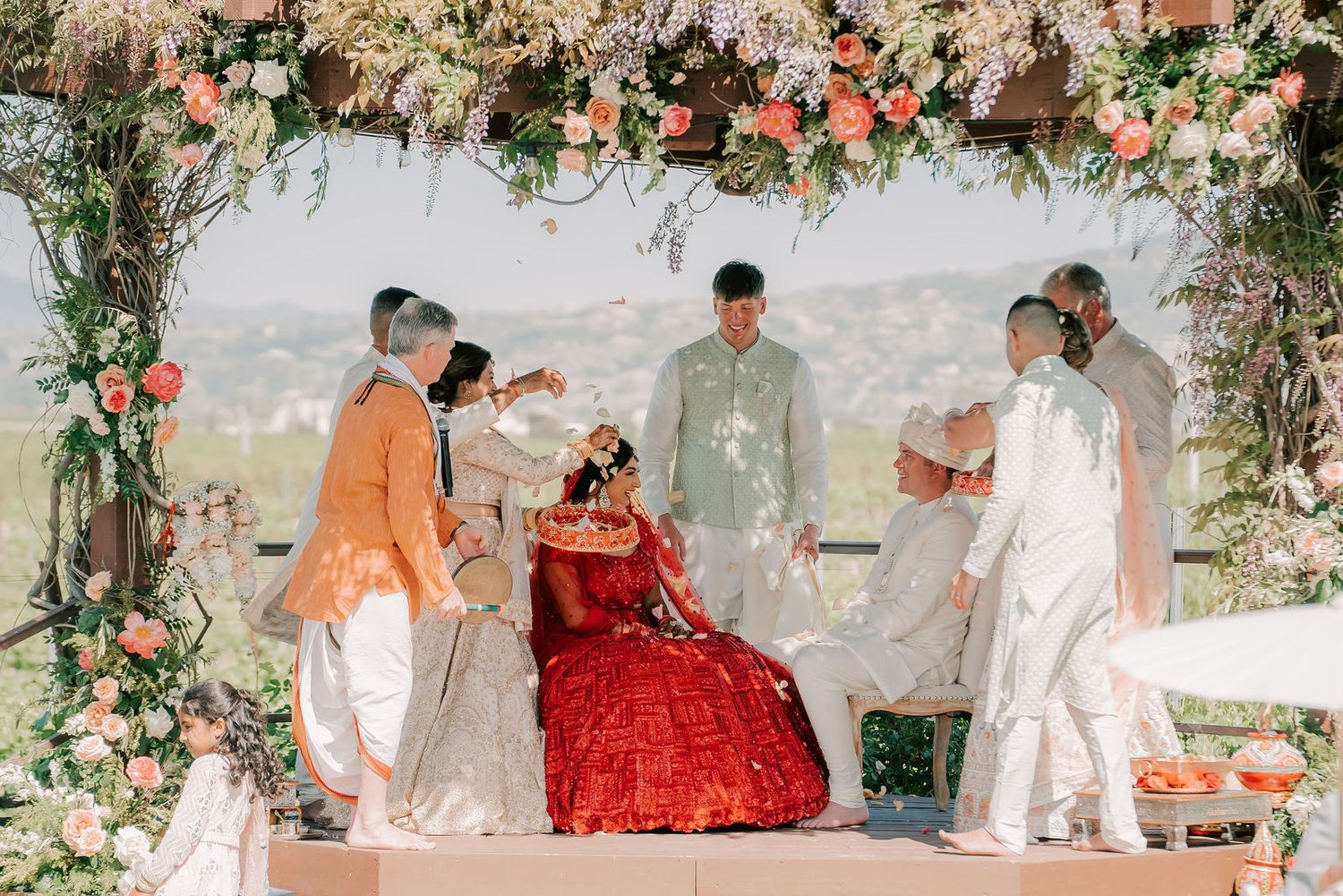 Traditional Indian wedding ceremony under ornate floral mandap with bride in red and groom in white.