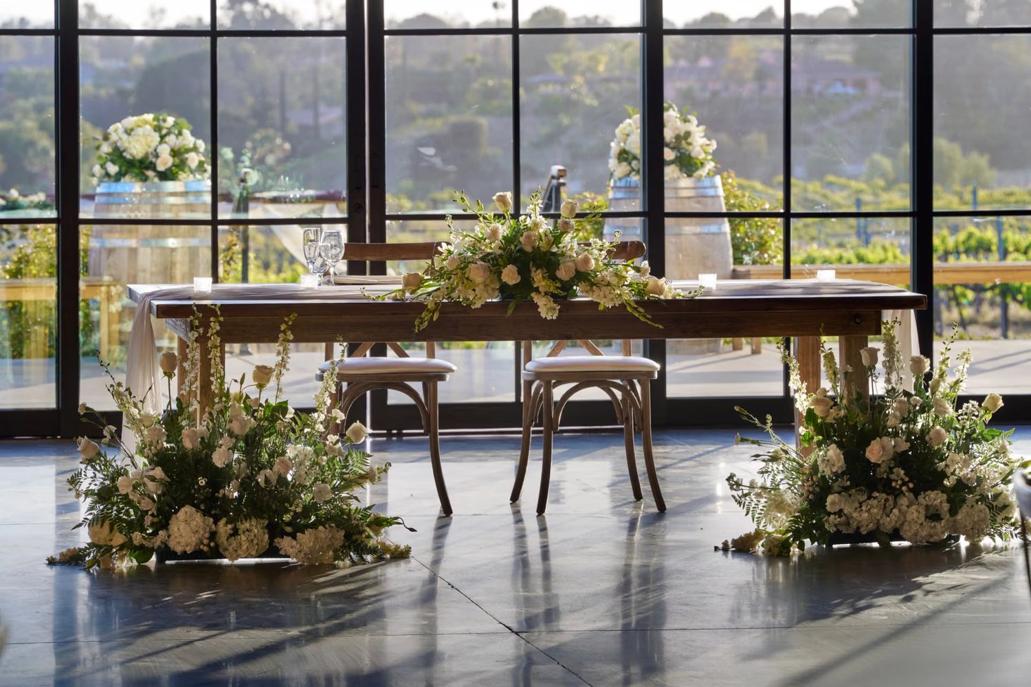 Elegant wedding sweetheart table adorned with lush floral arrangements and candles, set before large windows with garden views.