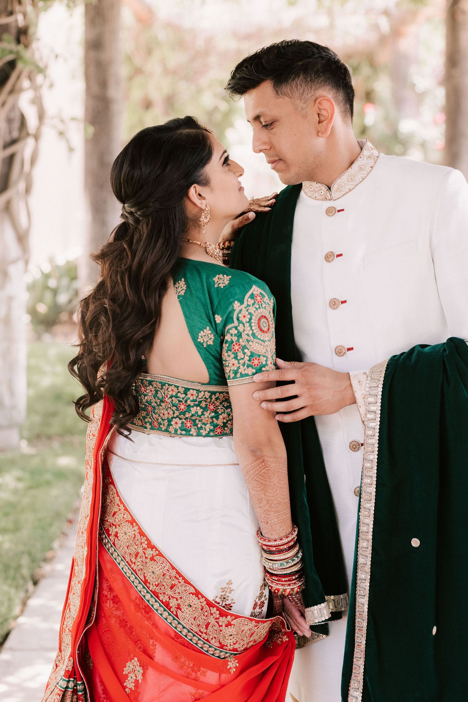 Indian couple in coordinating green and white traditional wedding outfits sharing intimate moment outdoors.