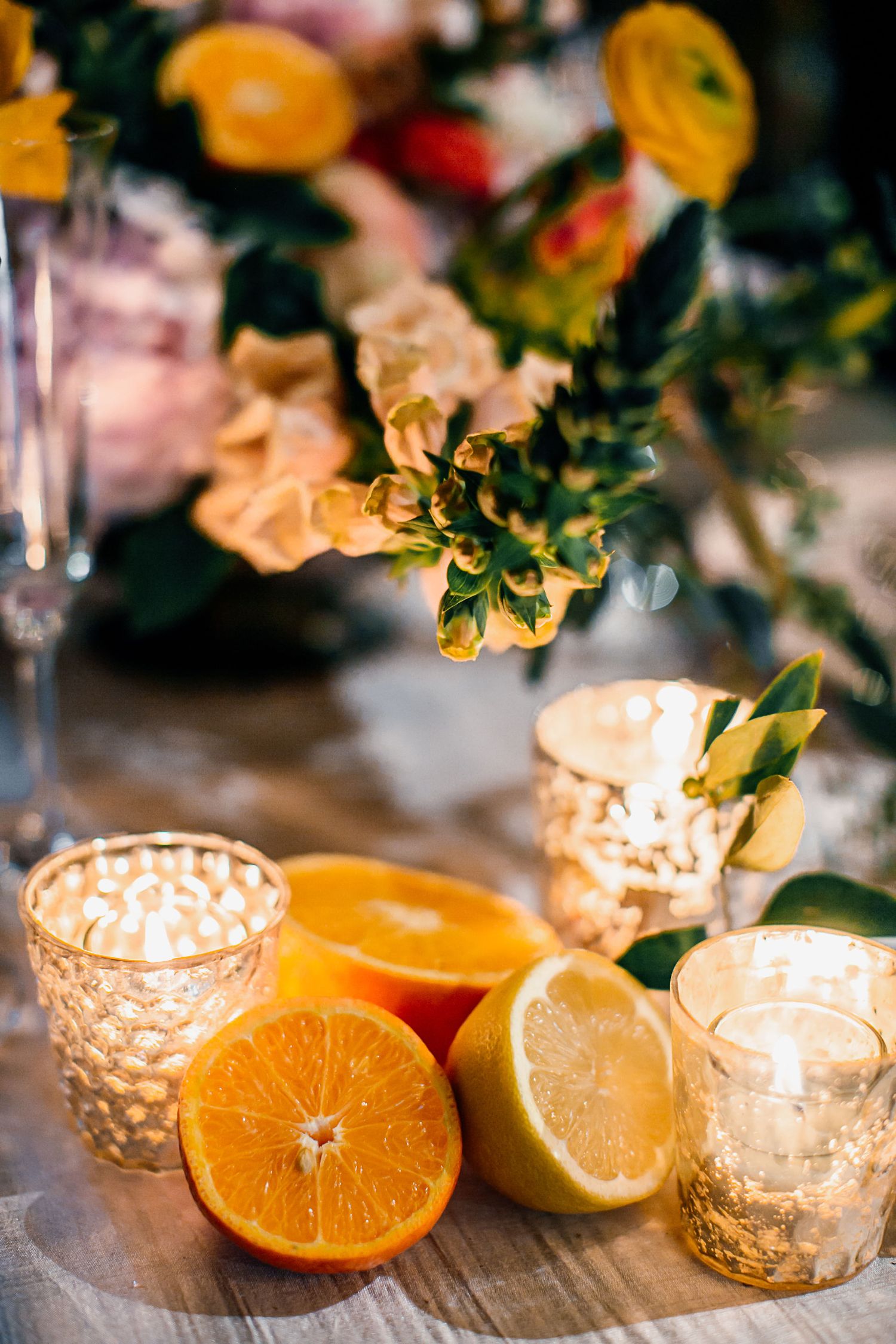 Sliced oranges and lemons arranged with glowing candles and colorful floral centerpiece on a wooden table.