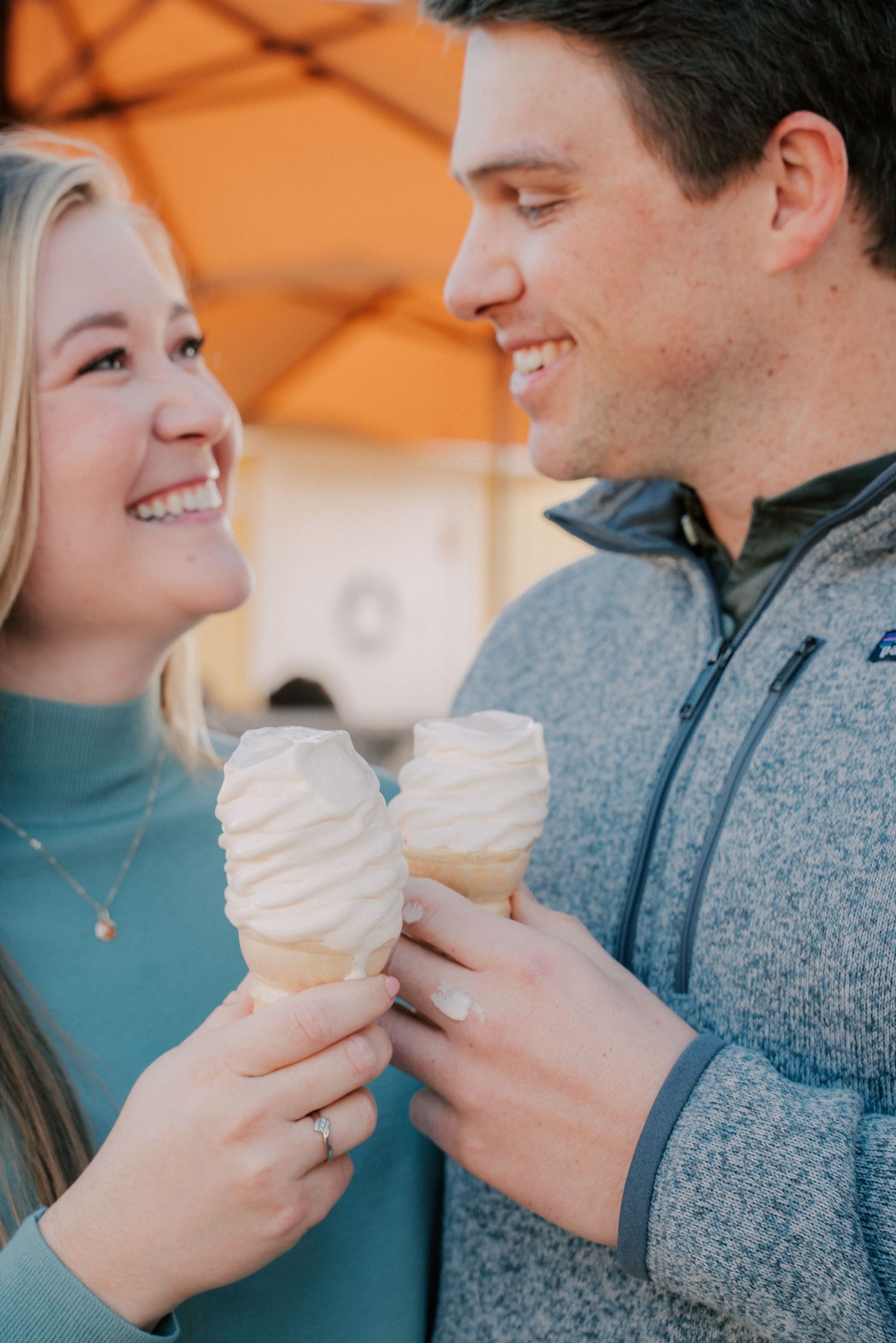 Smiling couple holding soft serve ice cream cones together, sharing a joyful moment outdoors.