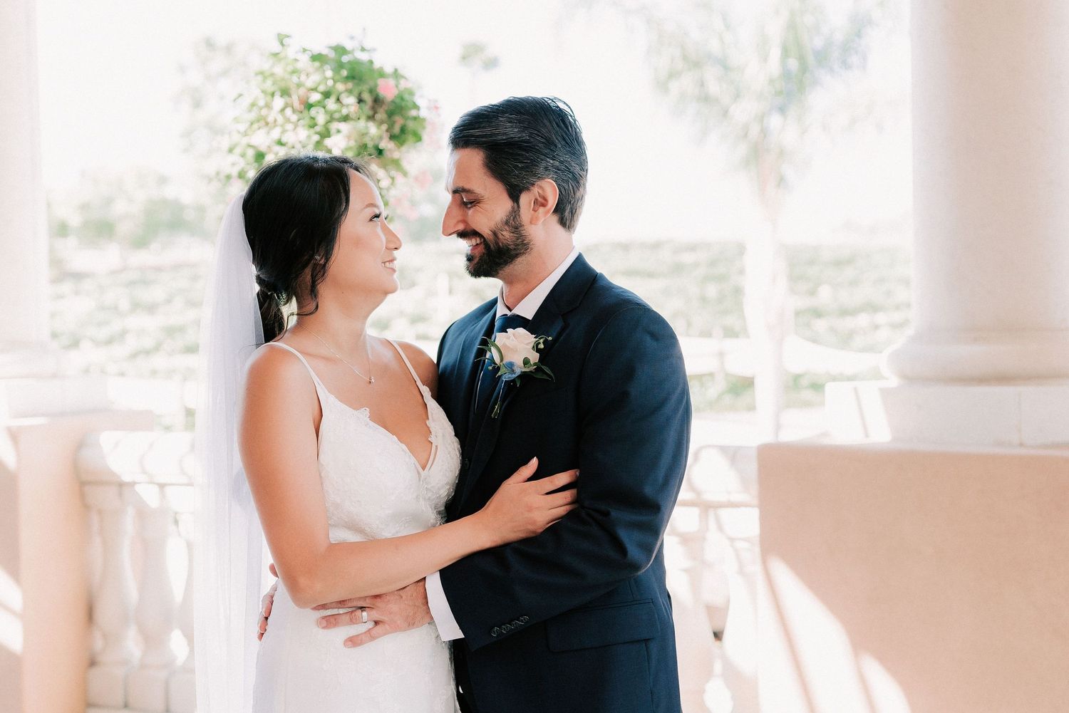 Bride and groom share a romantic moment outdoors, with the groom in a navy suit and bride in a white gown.