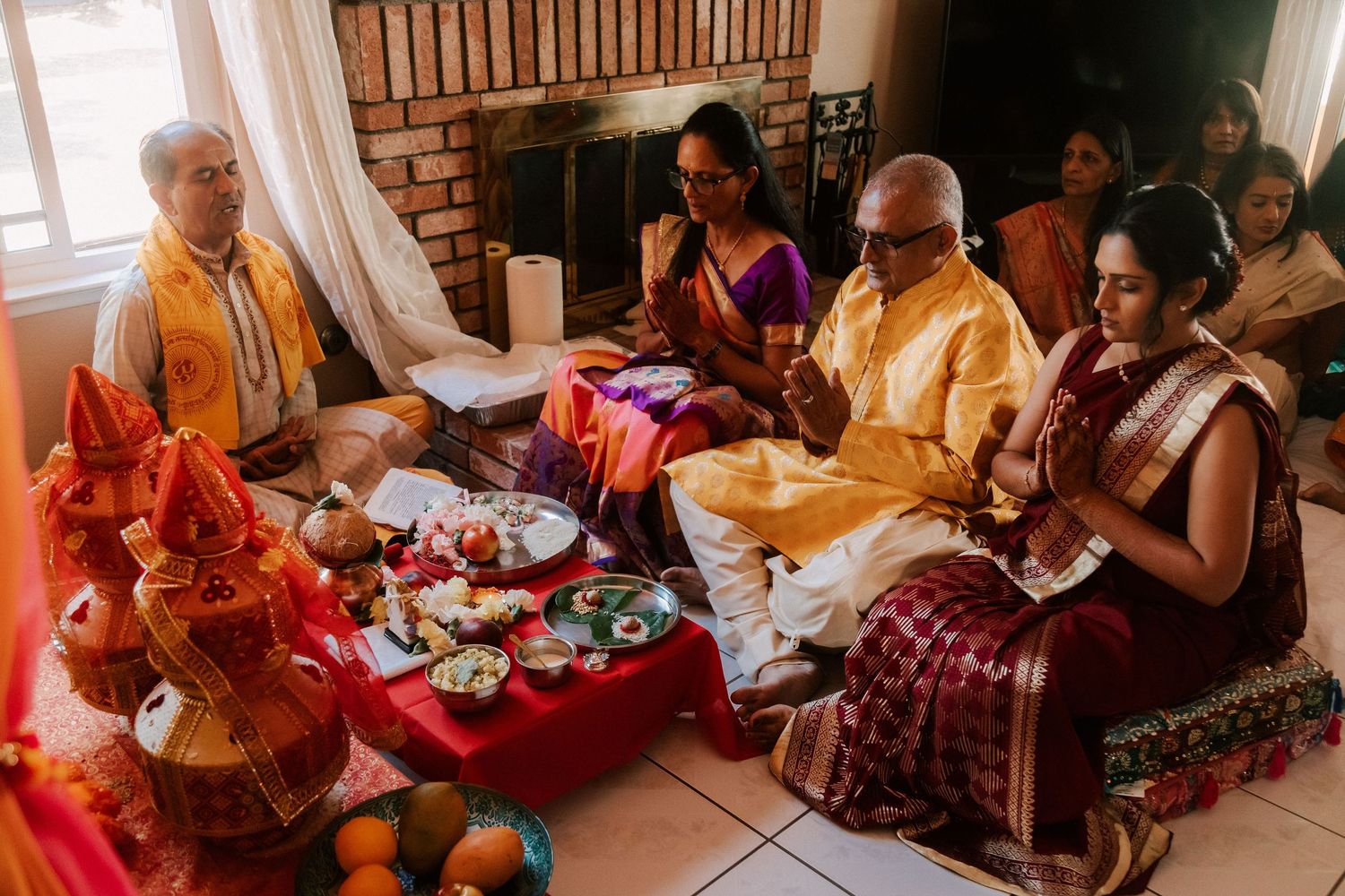 Family members in traditional Indian attire performing puja ceremony with offerings and decorations.