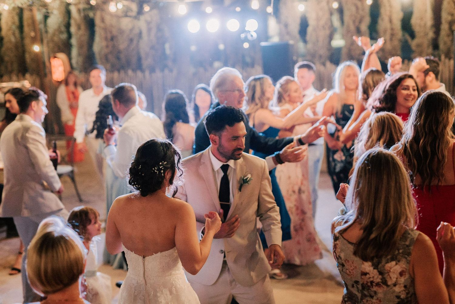 Bride and groom share a dance surrounded by guests at a warmly lit wedding reception.