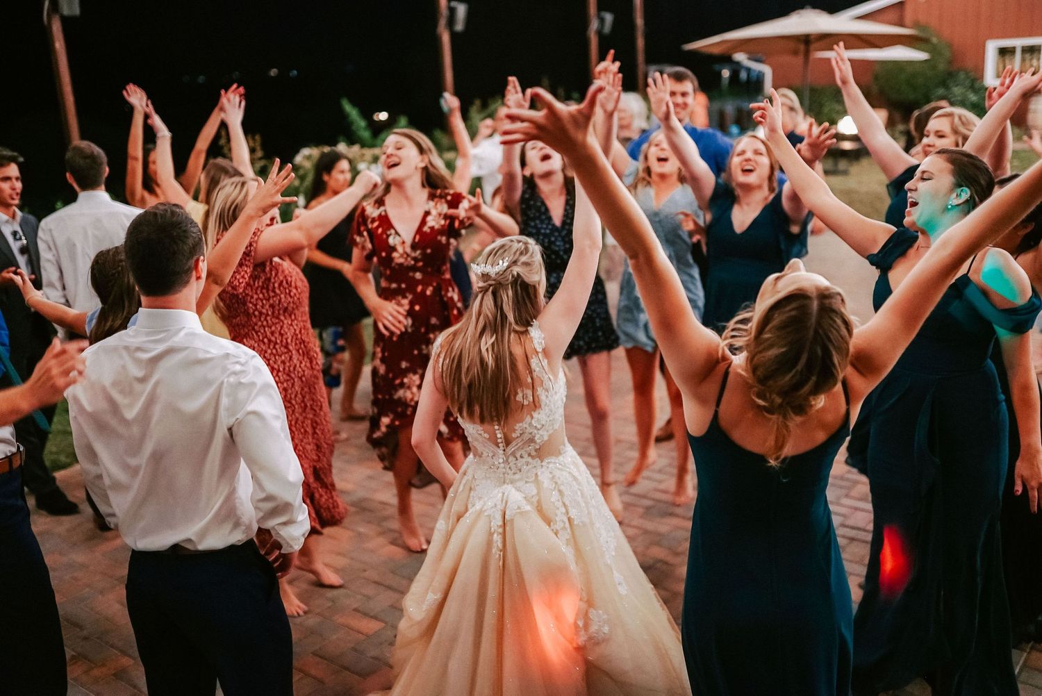 Bride in white gown dancing with guests at outdoor wedding reception celebration at night.