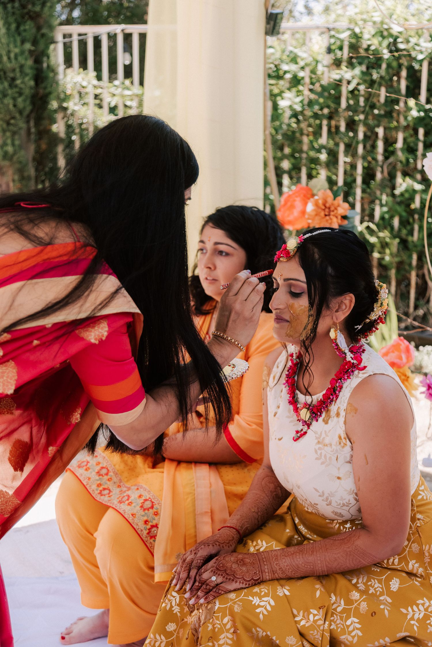 Woman applying haldi paste to brides face during traditional Indian haldi ceremony outdoors.