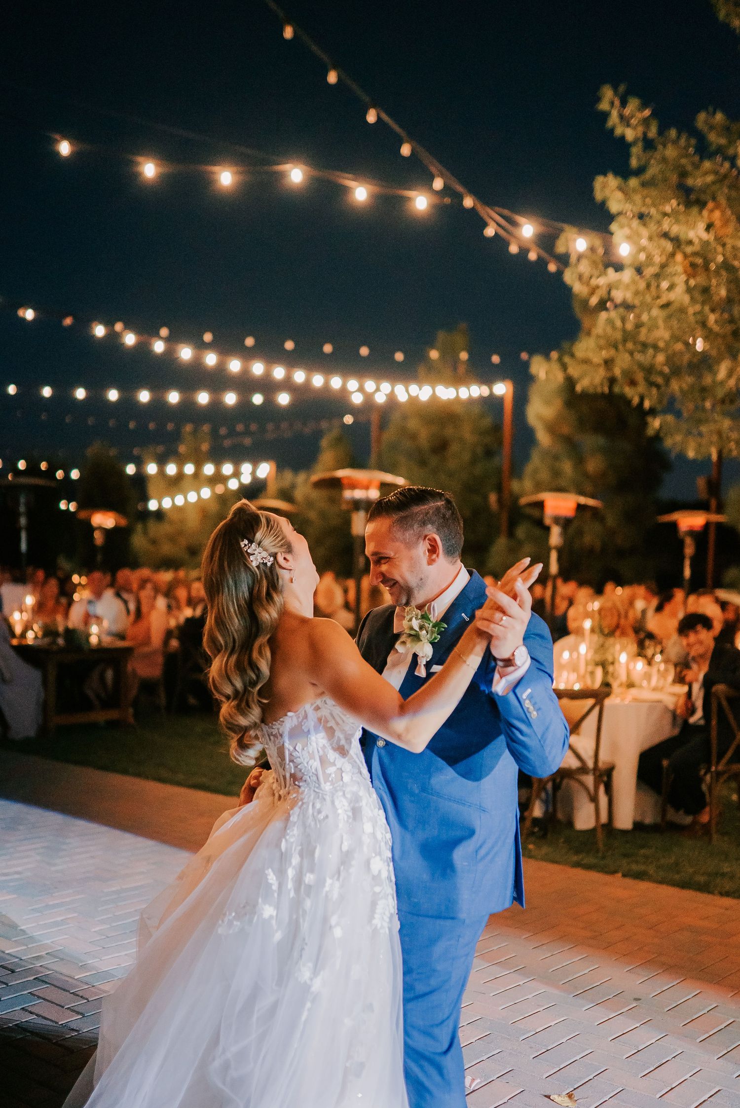 Bride and groom share first dance under string lights at outdoor wedding reception at night.