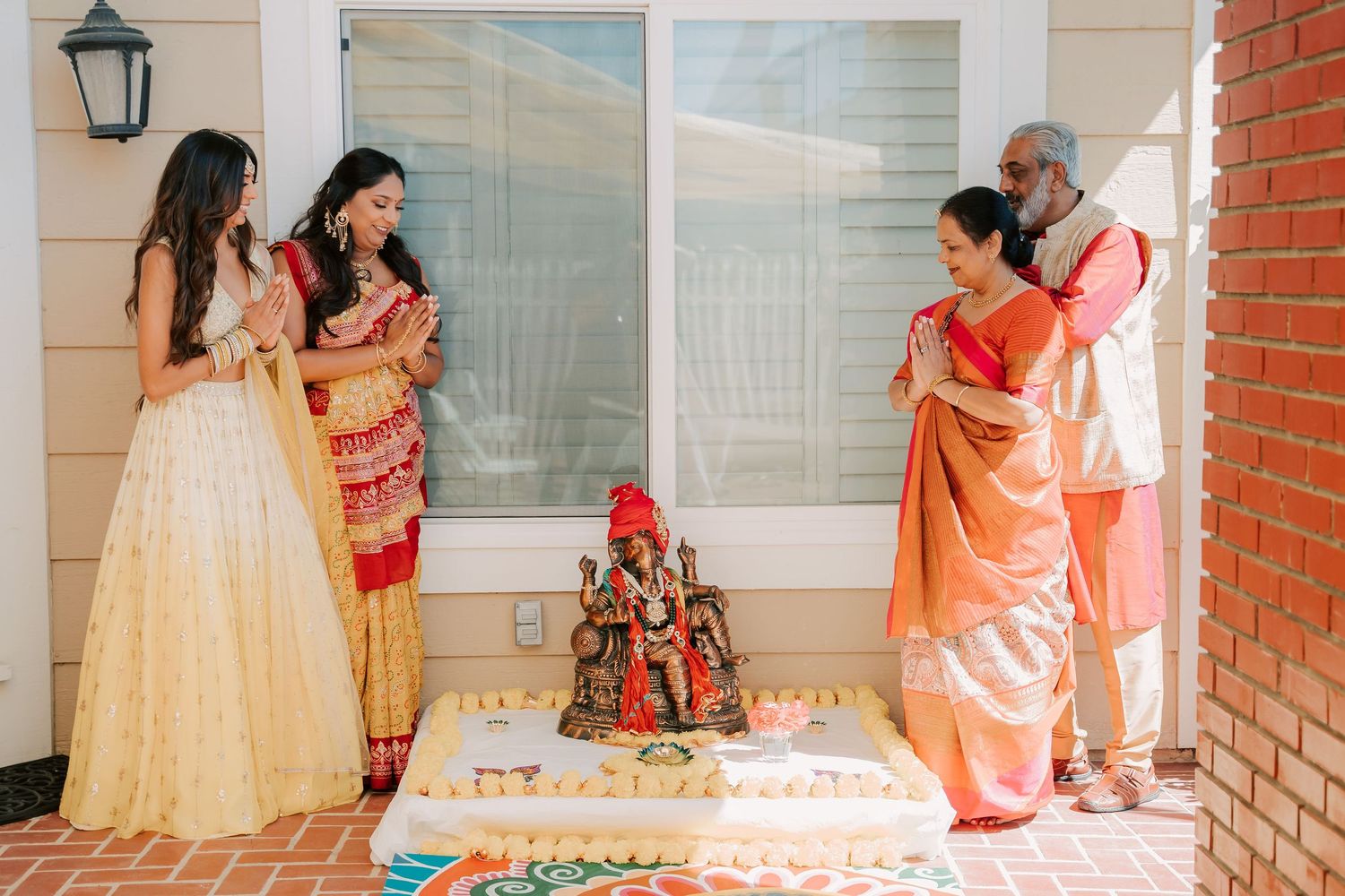 Indian family in traditional attire gathered around a Ganesh idol for a pre-wedding puja ceremony.