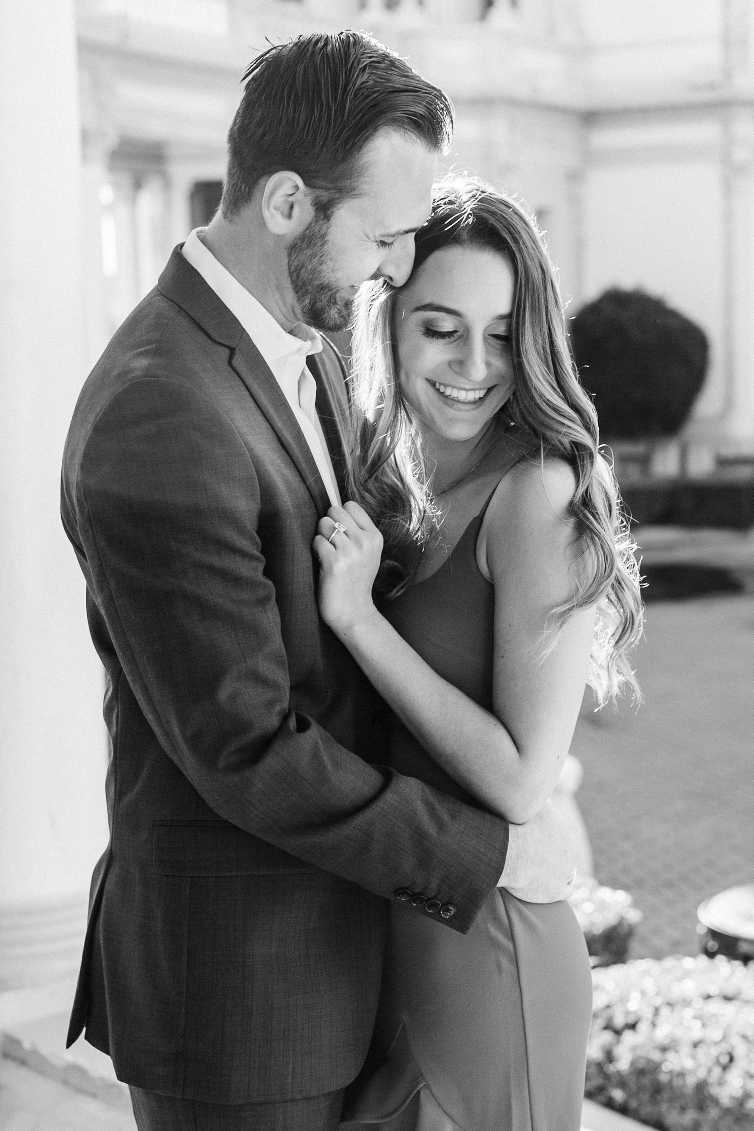 Black and white photo of a laughing couple embracing tenderly outside an elegant building.