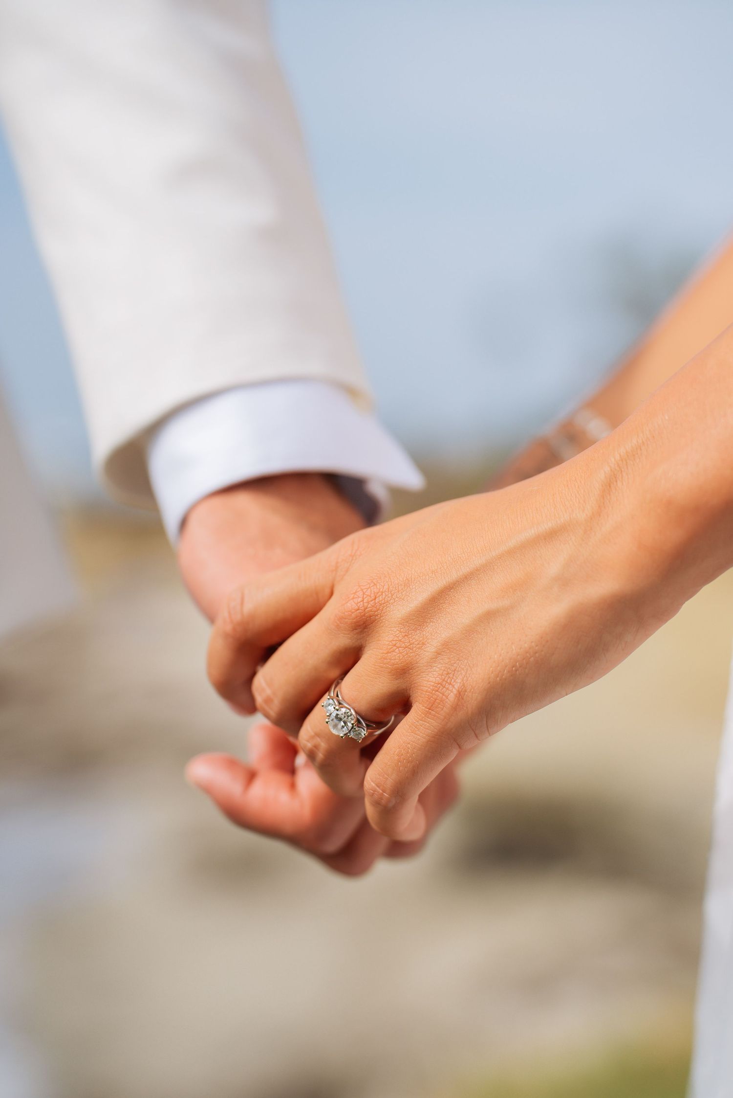 Close-up of bride and groom holding hands showing diamond engagement ring and wedding band.