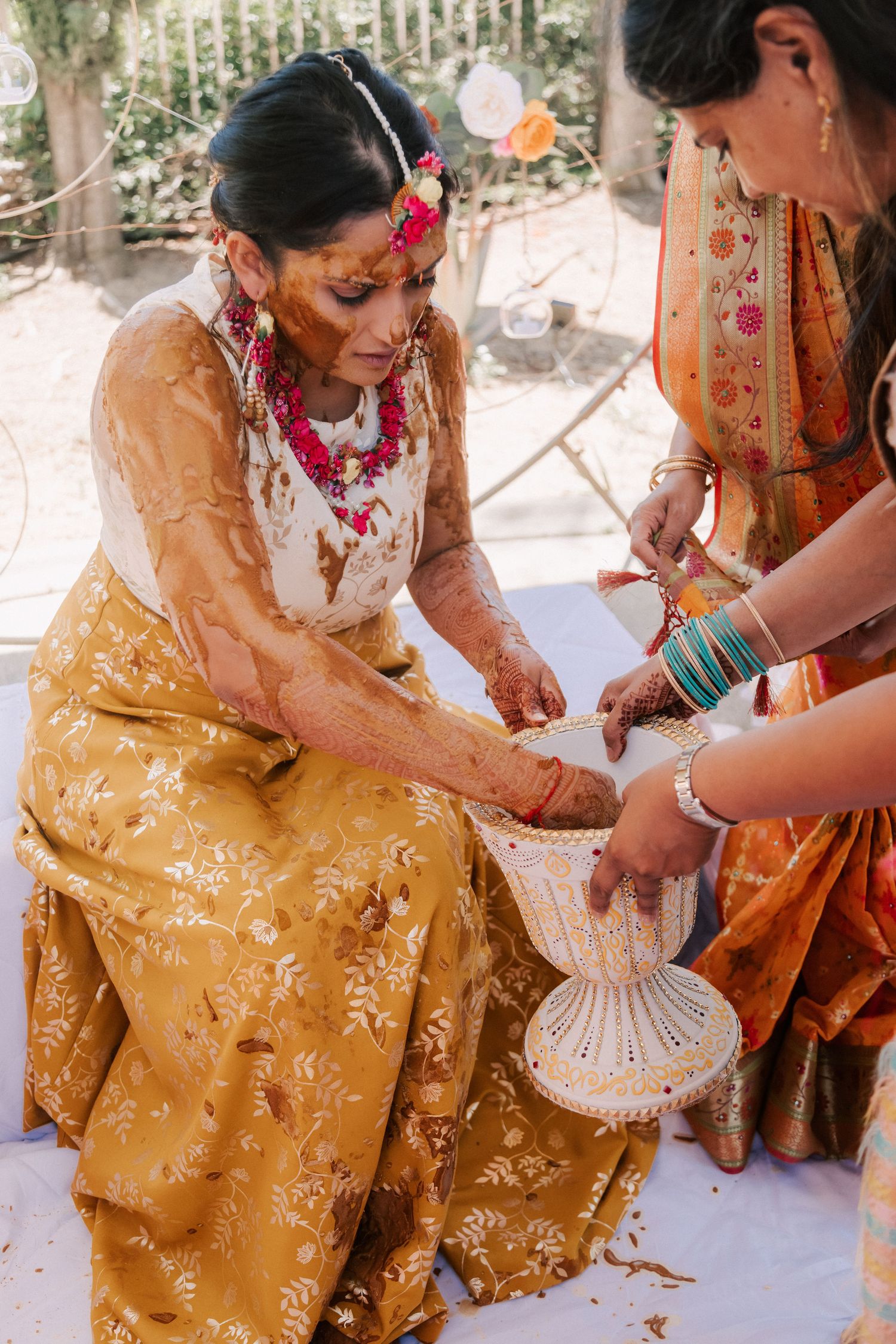 Bride in yellow floral lehenga with haldi paste applied during traditional Indian wedding ceremony.