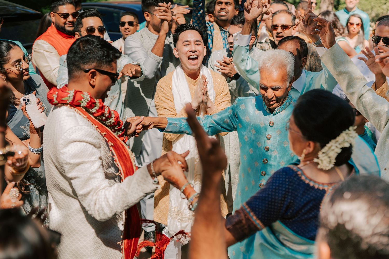 Groom dances joyfully with elderly relative and guests during lively Indian wedding baraat celebration.