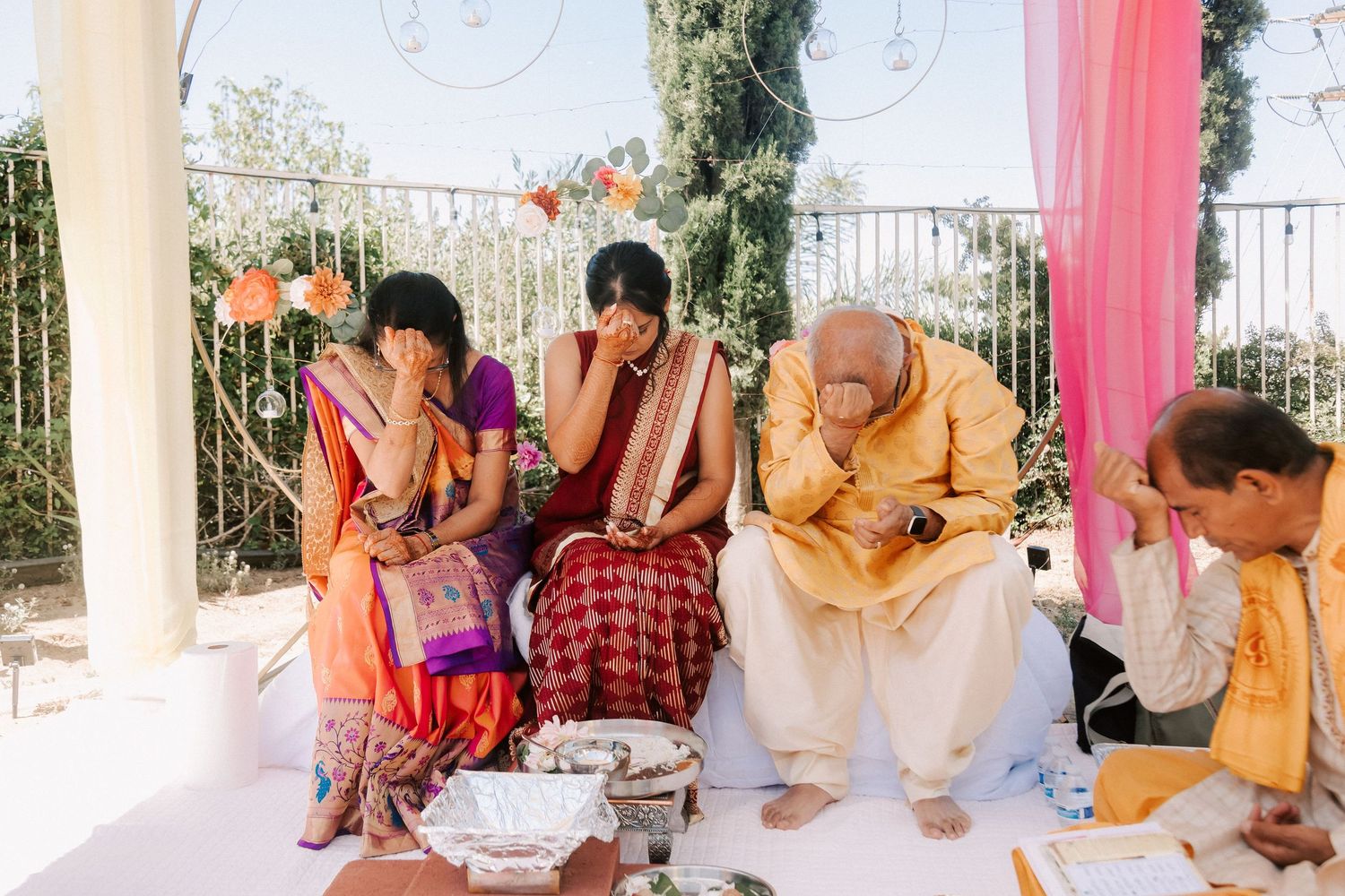 Family members in traditional Indian attire seated outdoors, emotional during a Hindu wedding ceremony ritual.