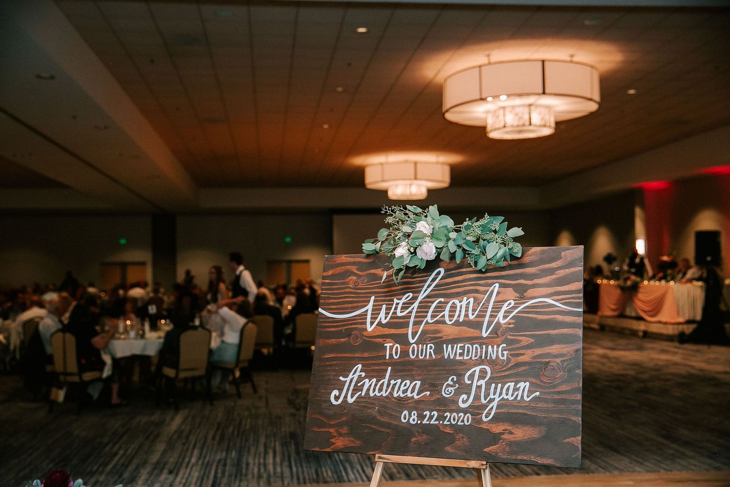 Rustic wooden wedding welcome sign for Andrea and Ryan dated 08.22.2020 with greenery in elegant ballroom.