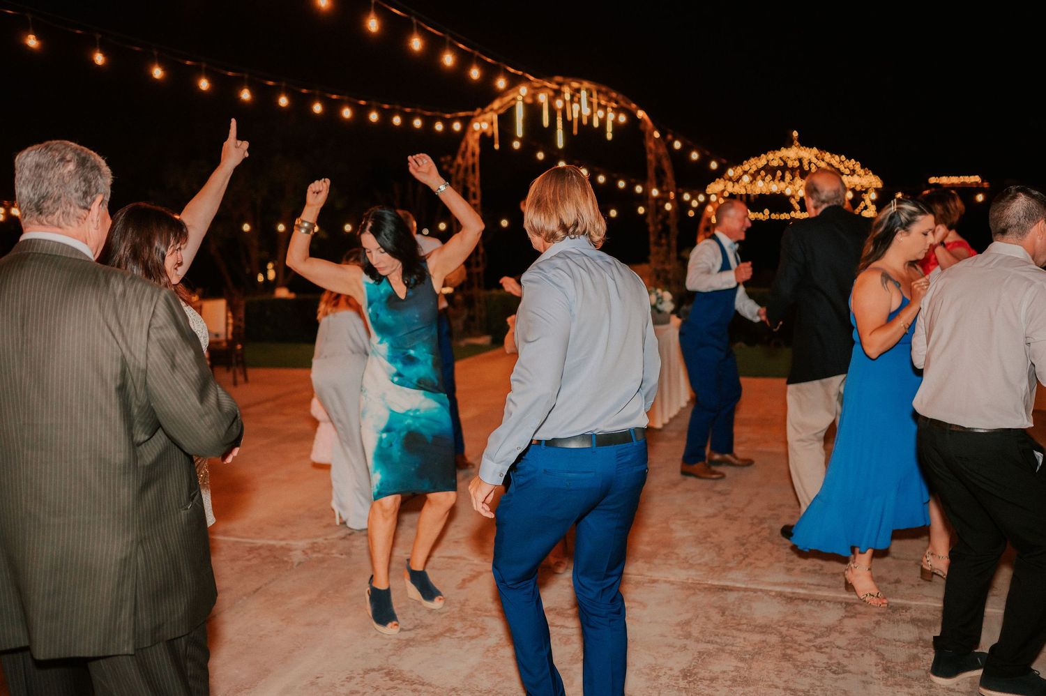 Guests dancing outdoors at night under string lights at a festive wedding reception celebration.