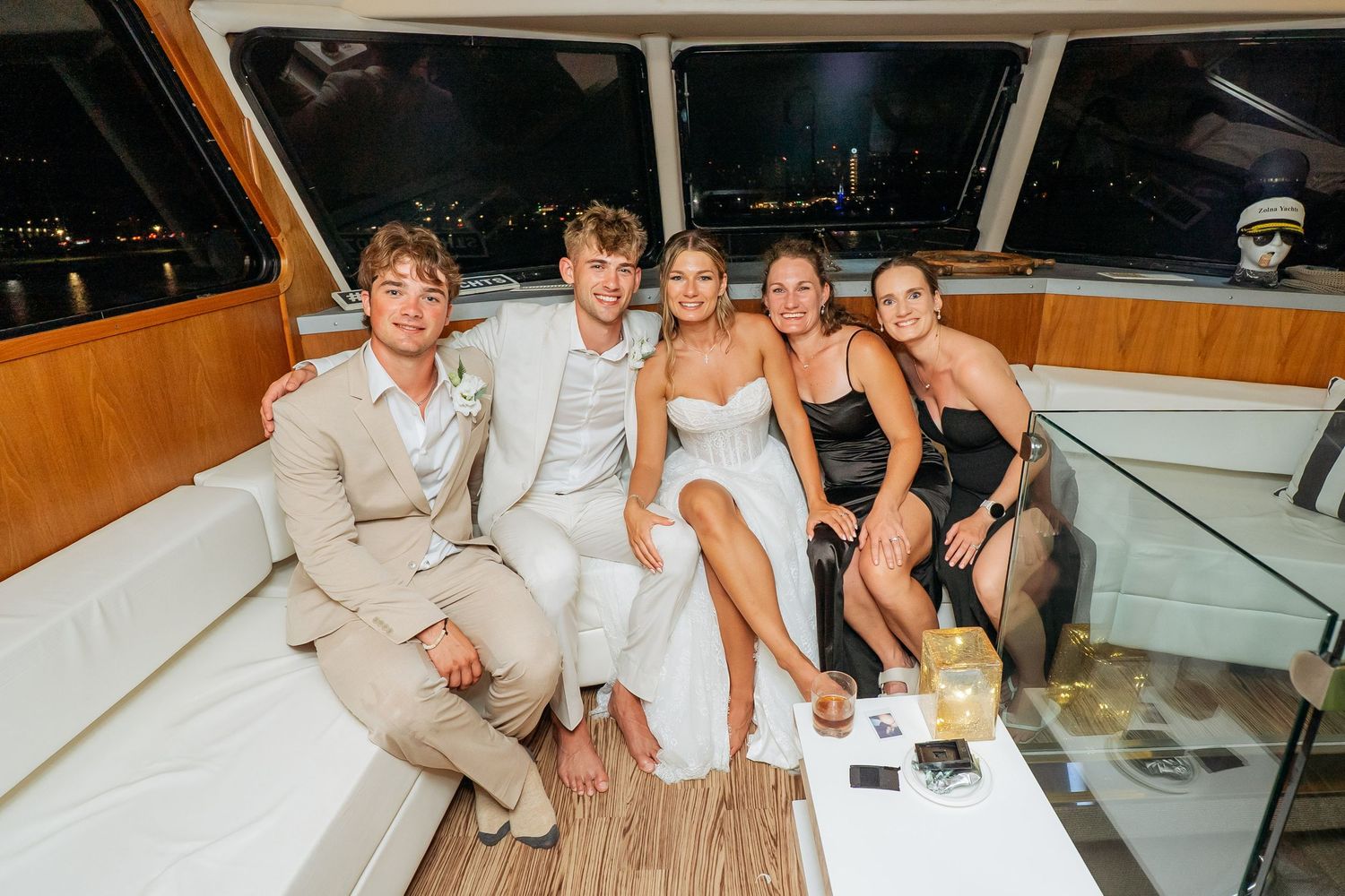 Wedding party posing on a luxury yacht at night, bride in white dress with guests in formal attire.