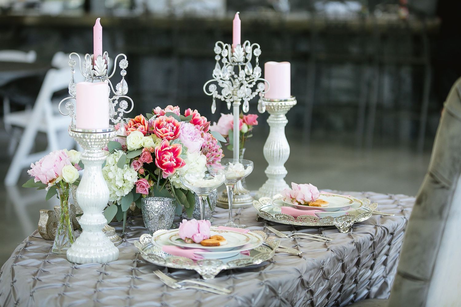 Elegant wedding tablescape with white candelabras, pink candles, floral centerpiece, and decorative plates on gray linen.