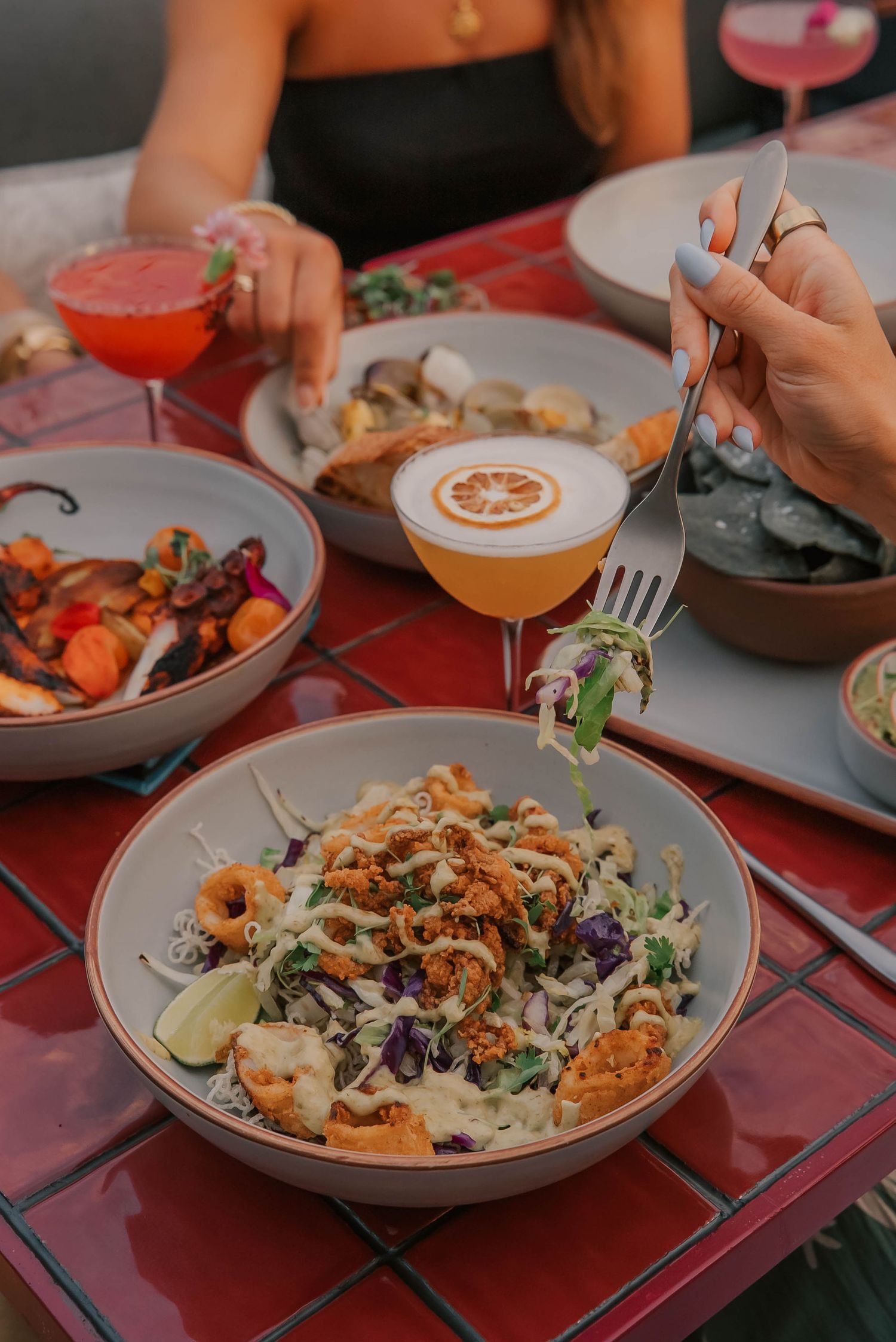 Colorful restaurant table with shrimp salad, cocktails, and seafood dishes being enjoyed by two women dining out.
