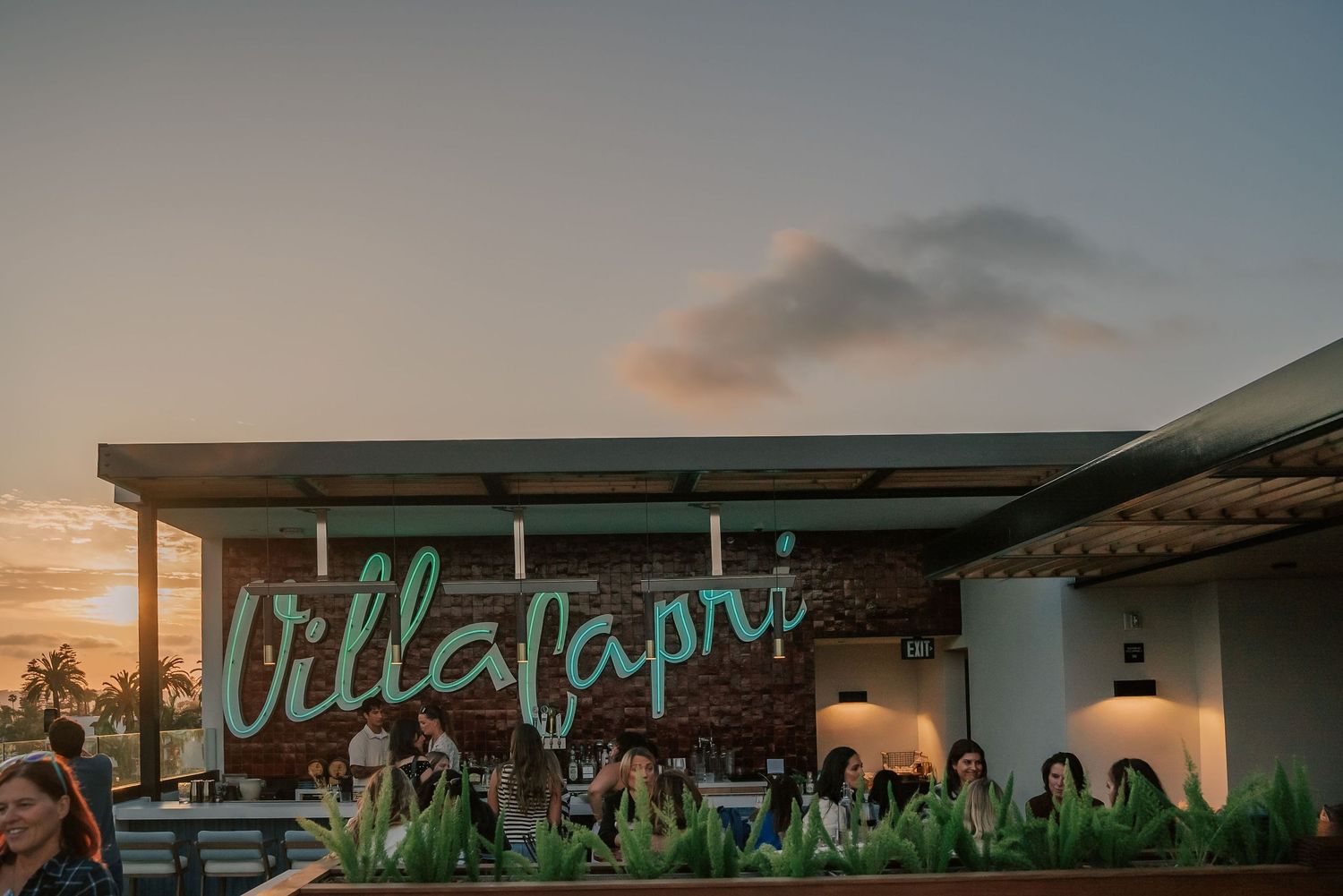 Villa Capri restaurant exterior sign glowing at sunset with guests dining on outdoor patio terrace.