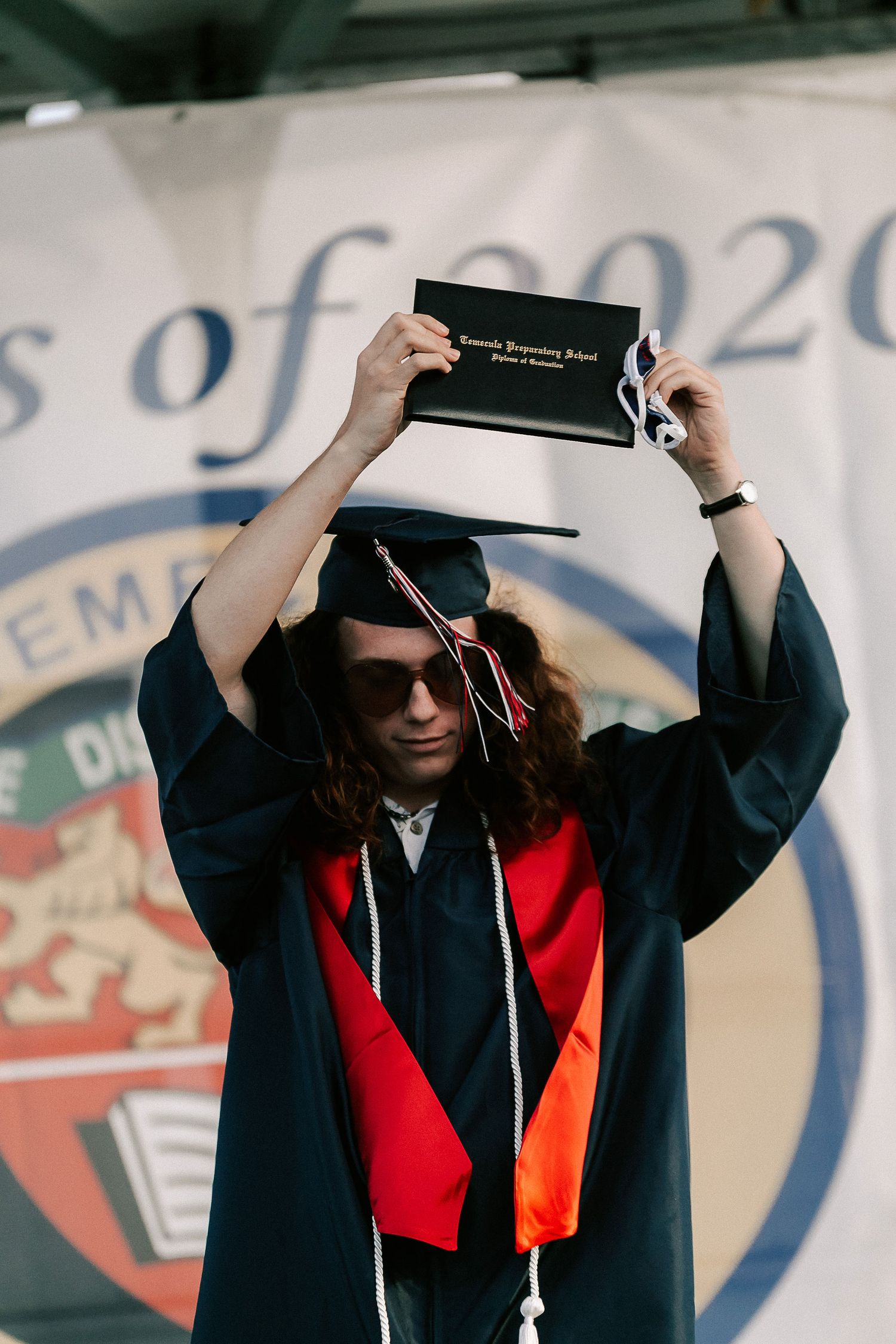 Graduate in cap and gown holds diploma above head at Class of 2020 commencement ceremony.