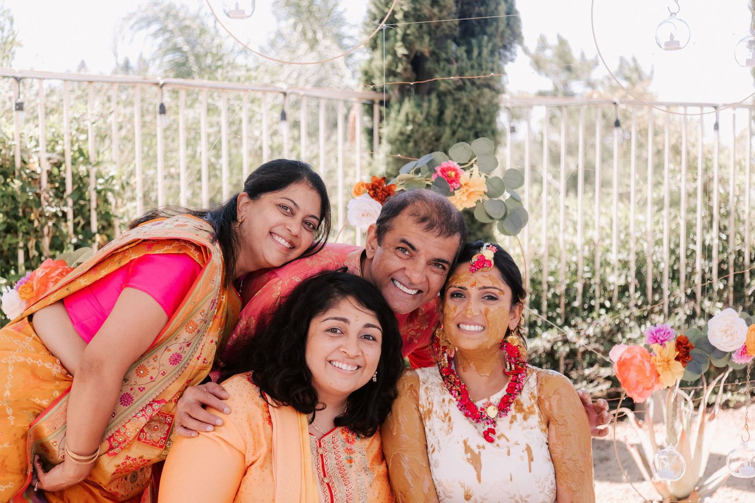Happy family of four posing together outdoors during colorful Indian haldi wedding celebration.