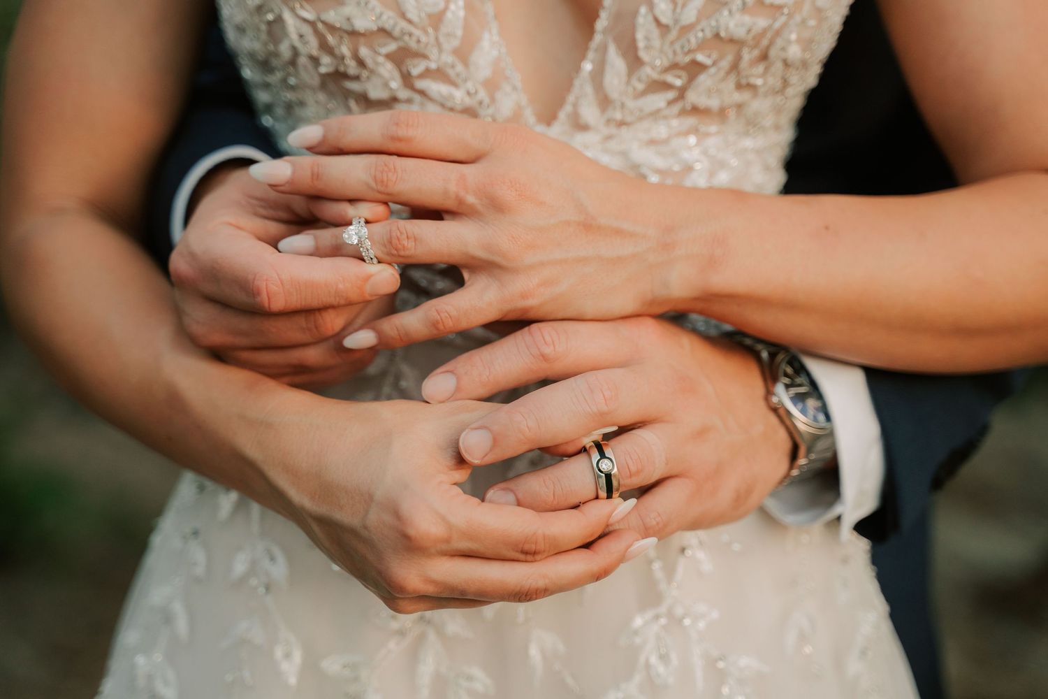 Bride and groom holding hands showing wedding rings, close-up of couple exchanging bands in elegant attire.