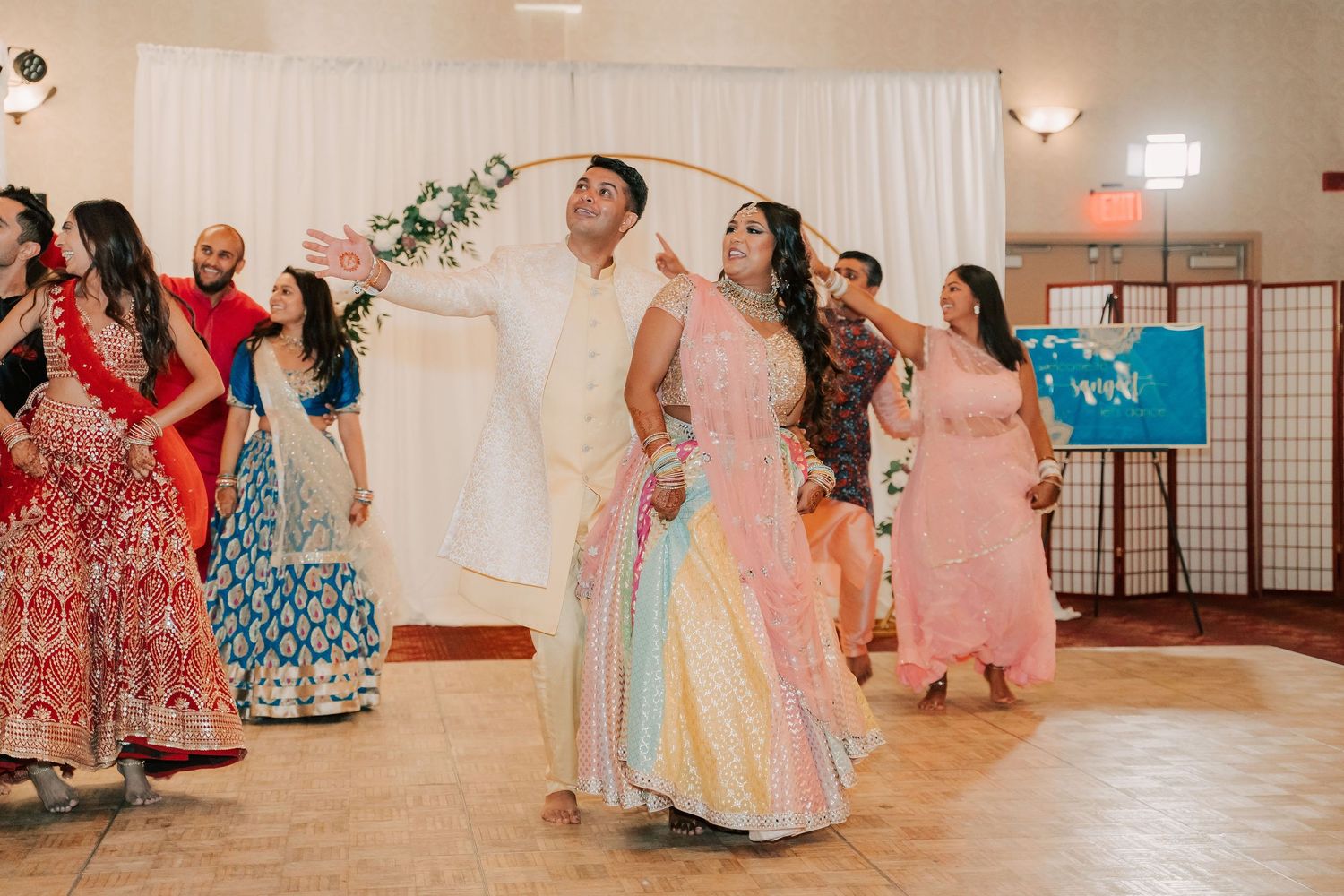 Couple dancing in colorful traditional Indian attire at a vibrant wedding reception celebration.