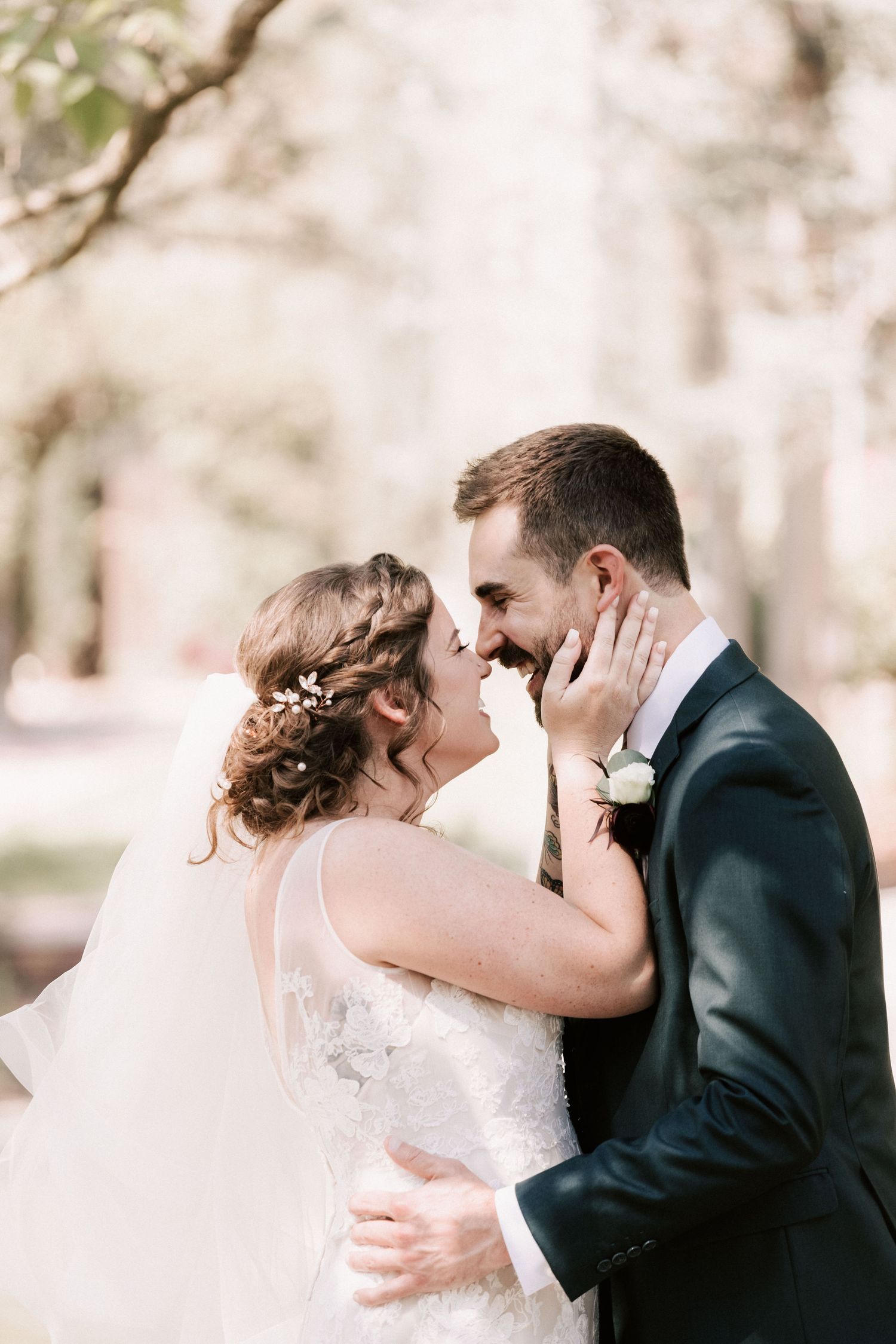 Bride and groom share a romantic almost-kiss moment outdoors, with bride in lace gown and groom in dark suit with boutonniere.