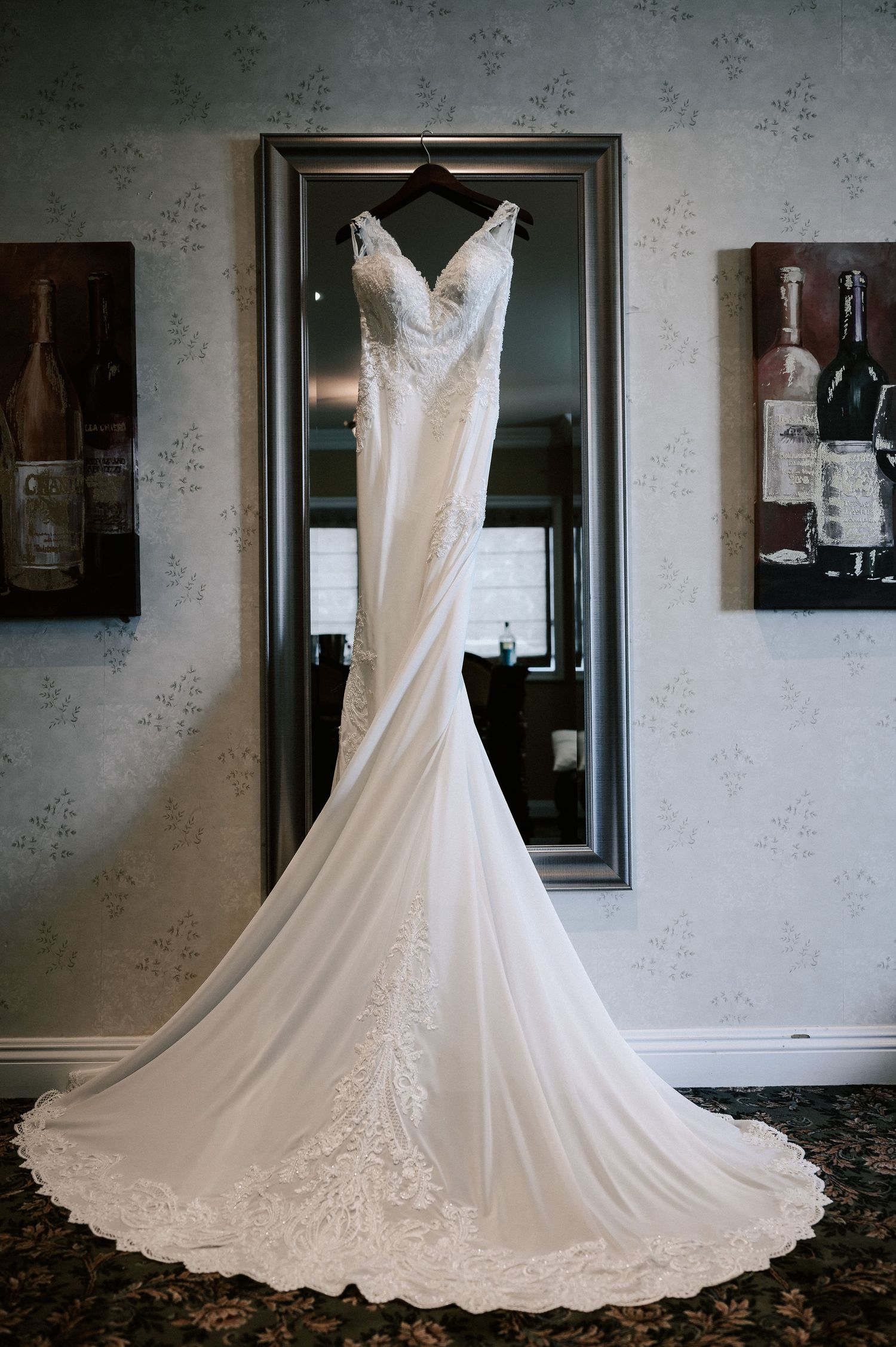 Elegant white lace mermaid wedding dress with a long train hanging on a mirror in a decorated room.