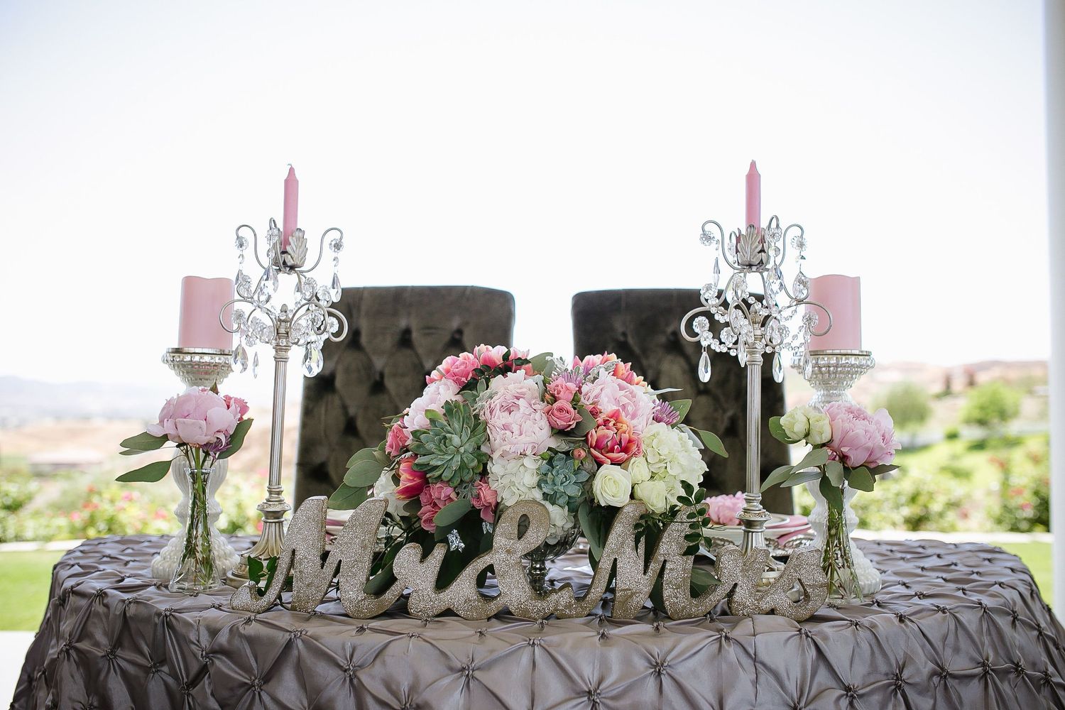 Elegant wedding sweetheart table with pink floral centerpiece, candelabras, and Mr & Mrs sign on gray pintuck linen.