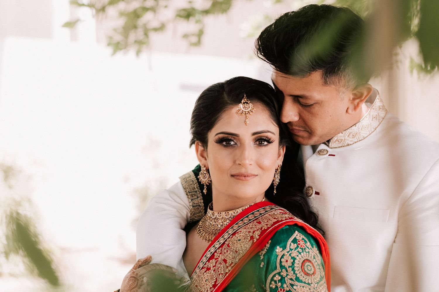 Indian bride and groom in traditional green and white wedding attire posing romantically.