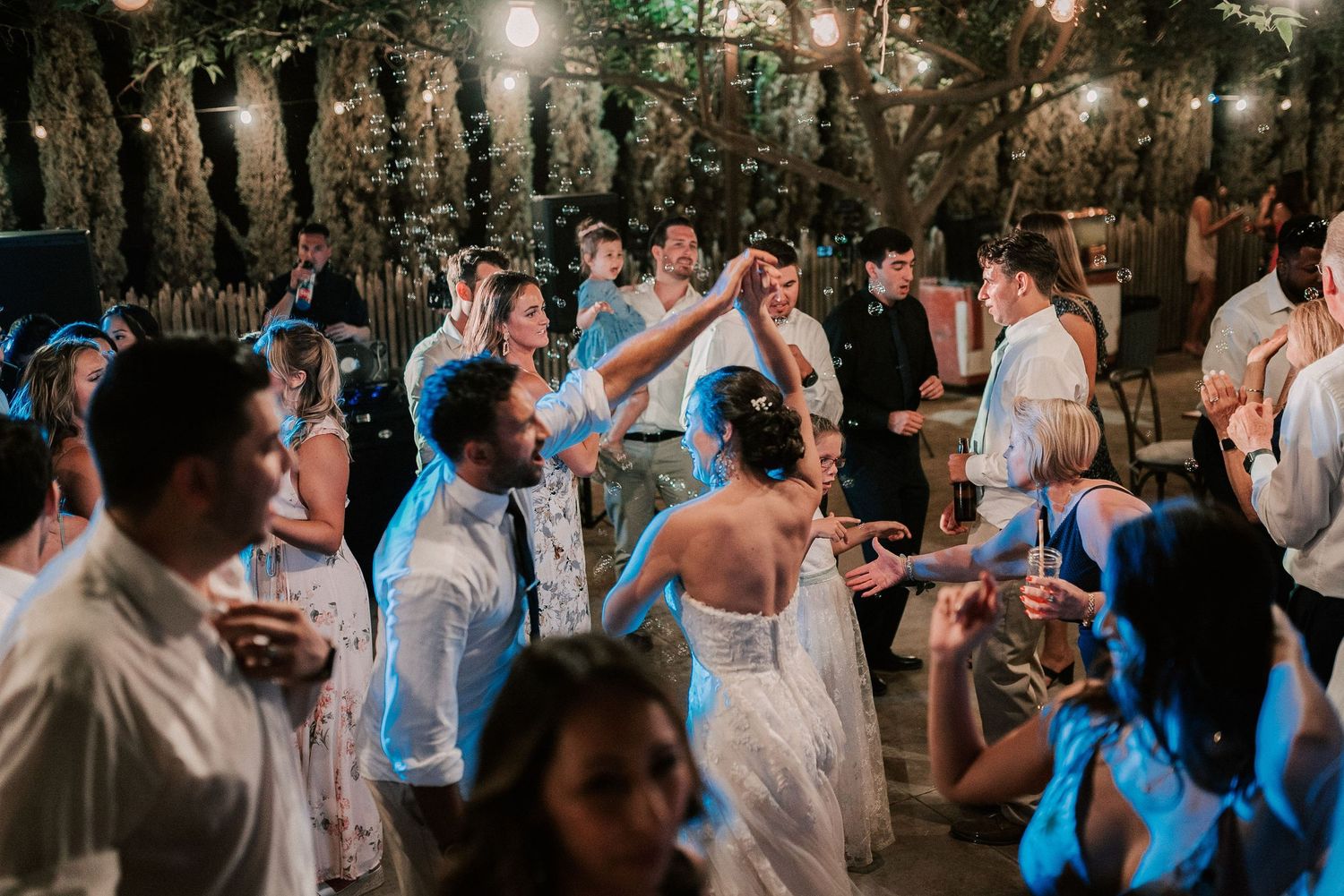 Guests dancing and celebrating at an outdoor wedding reception under string lights at night.